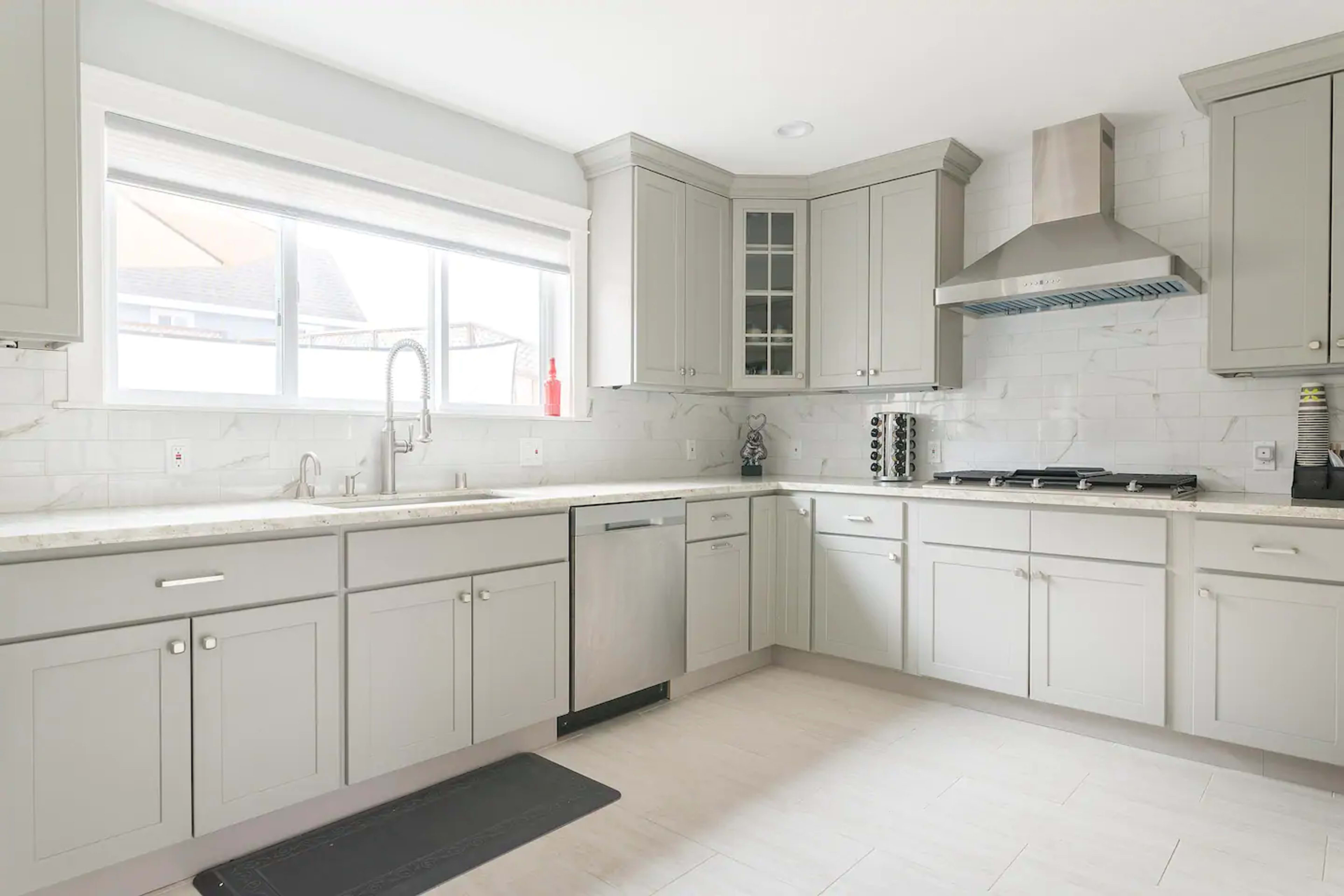 A modern kitchen features light gray cabinets, a stainless steel dishwasher, and a gas stove under a stainless steel range hood.