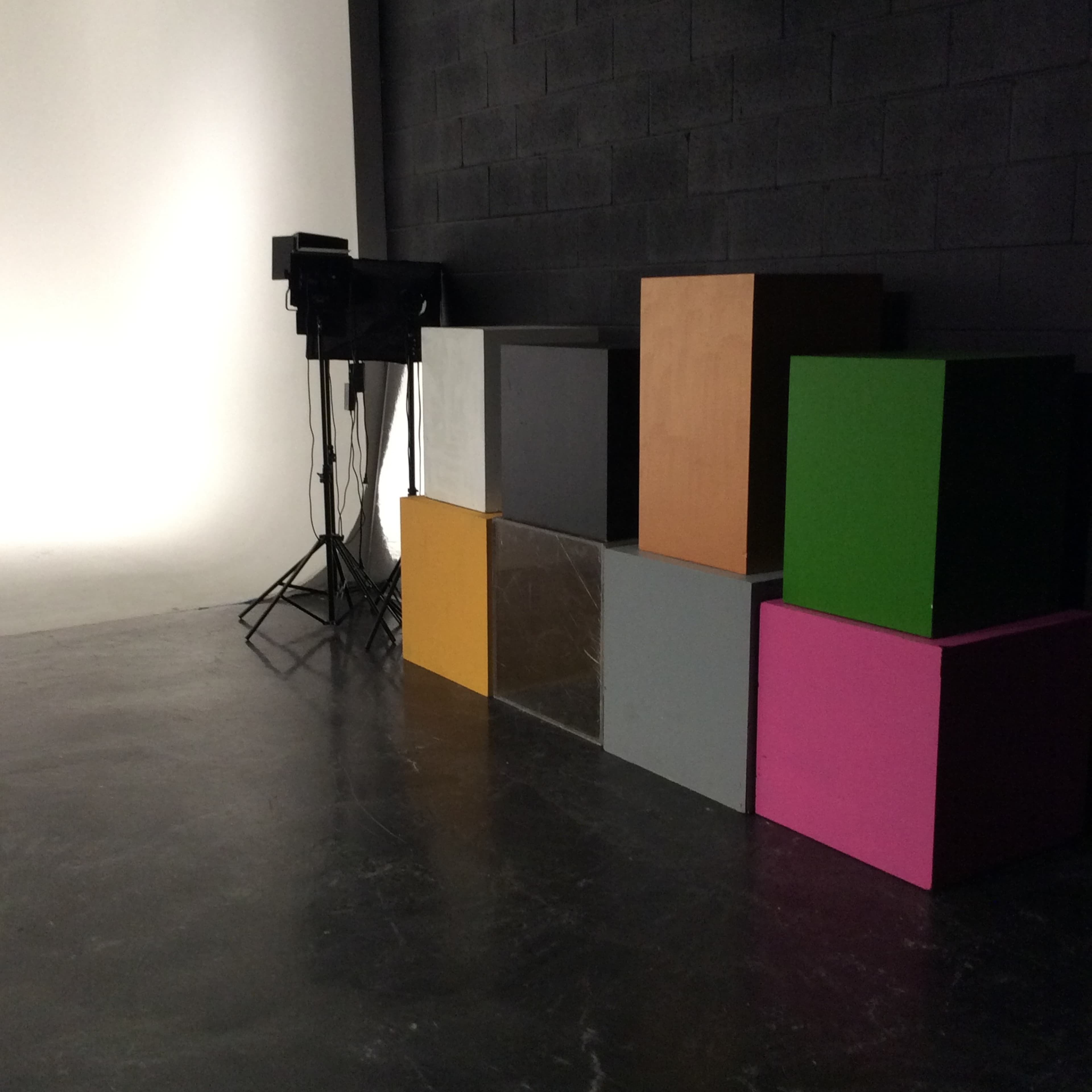 A series of stacked, colored cubes against a black wall, with lighting equipment positioned nearby.