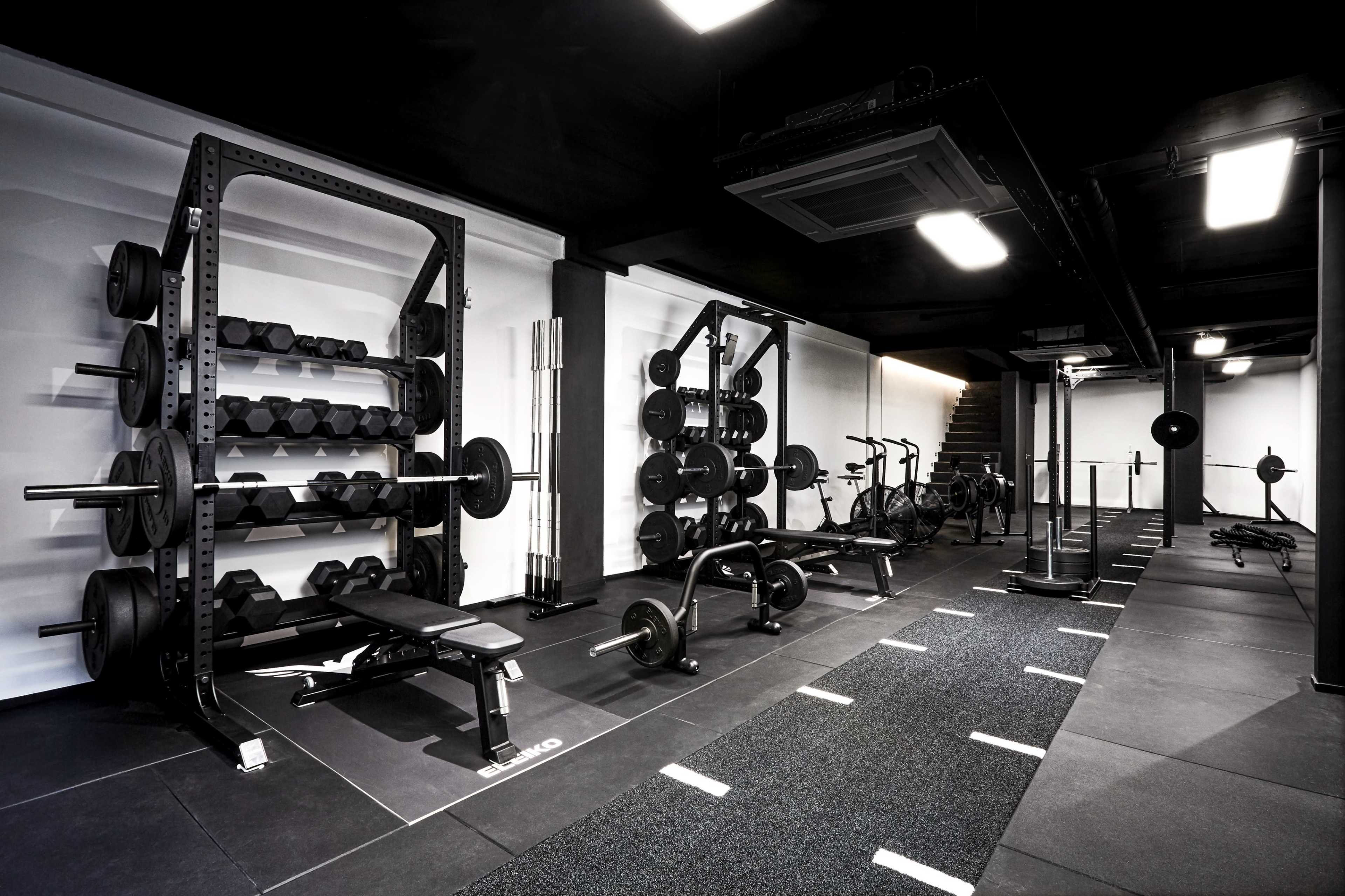 A modern gym layout with weight racks, benches, and various weightlifting equipment situated on black flooring.