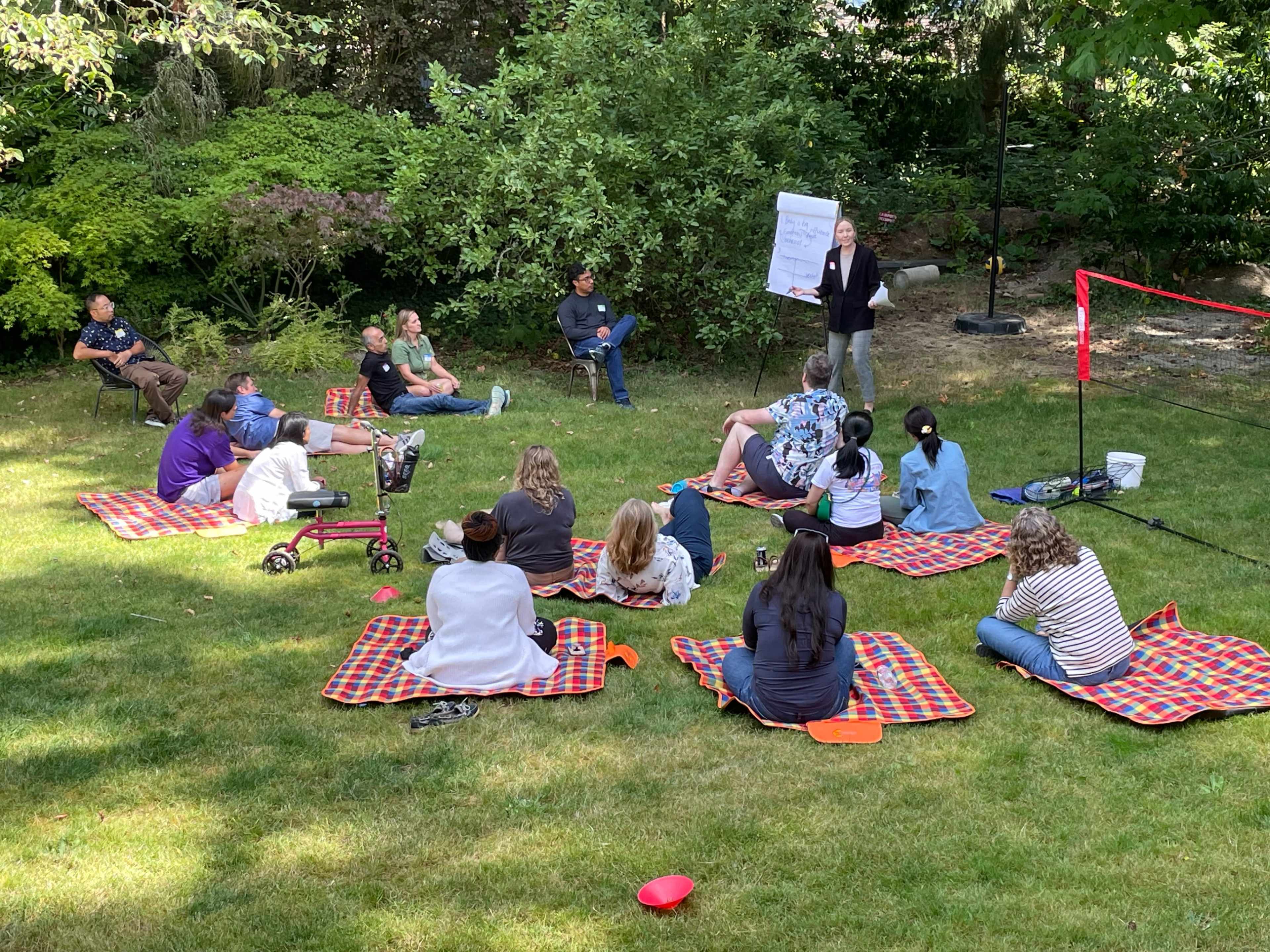 A group of people are gathered on picnic blankets in a grassy area for an outdoor presentation.