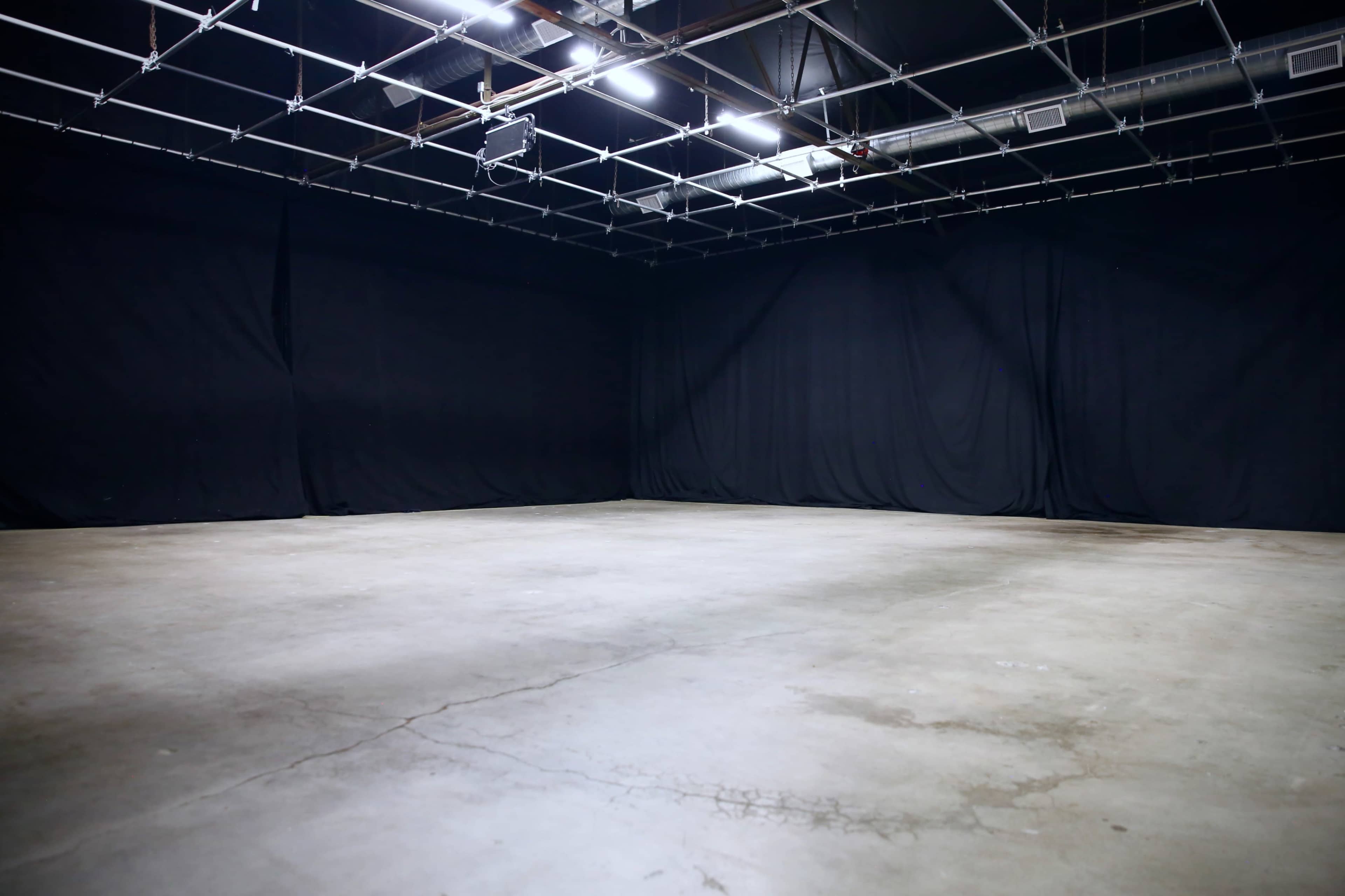 An empty studio space with a concrete floor and black fabric drapes covering the walls.