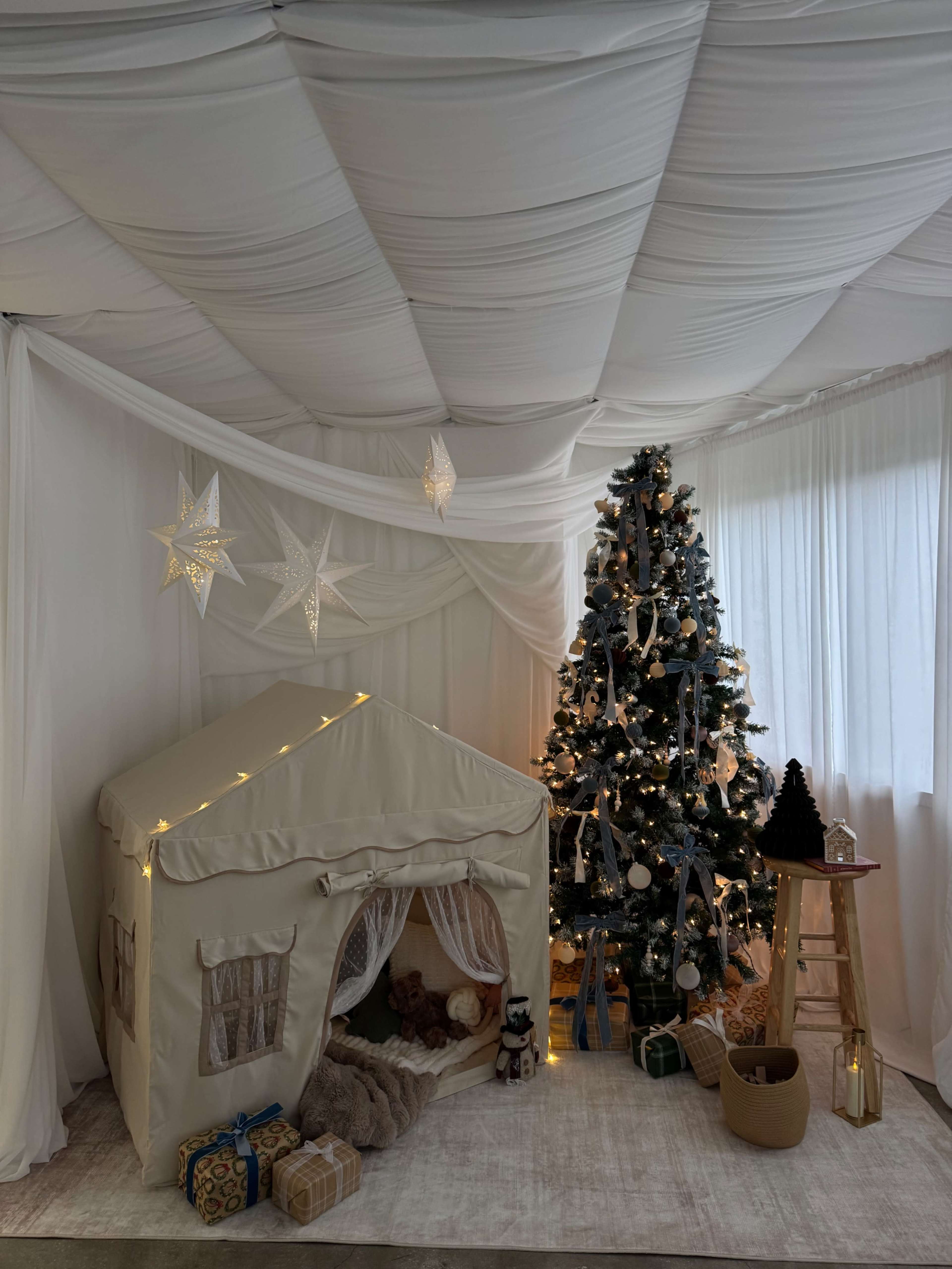 The scene features a cozy indoor space decorated with a Christmas tree, a tent-like play structure, and wrapped gifts.