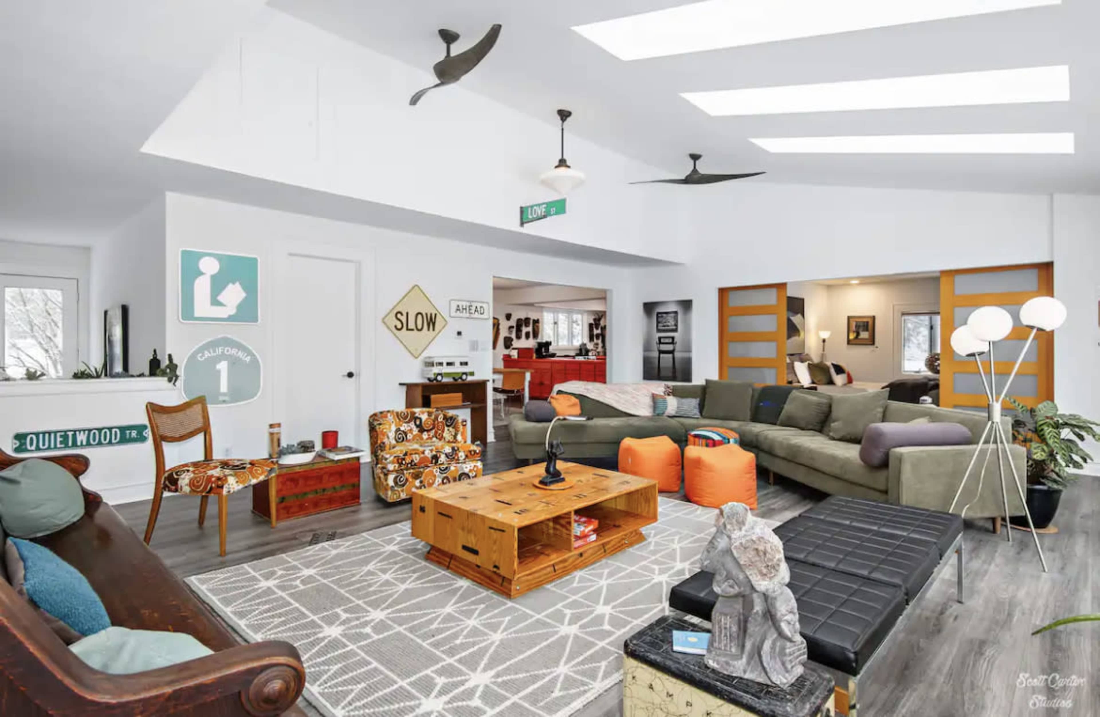 The living room features a mix of modern and vintage furniture, including a large sectional sofa, a wooden coffee table, and decorative signage on the walls.