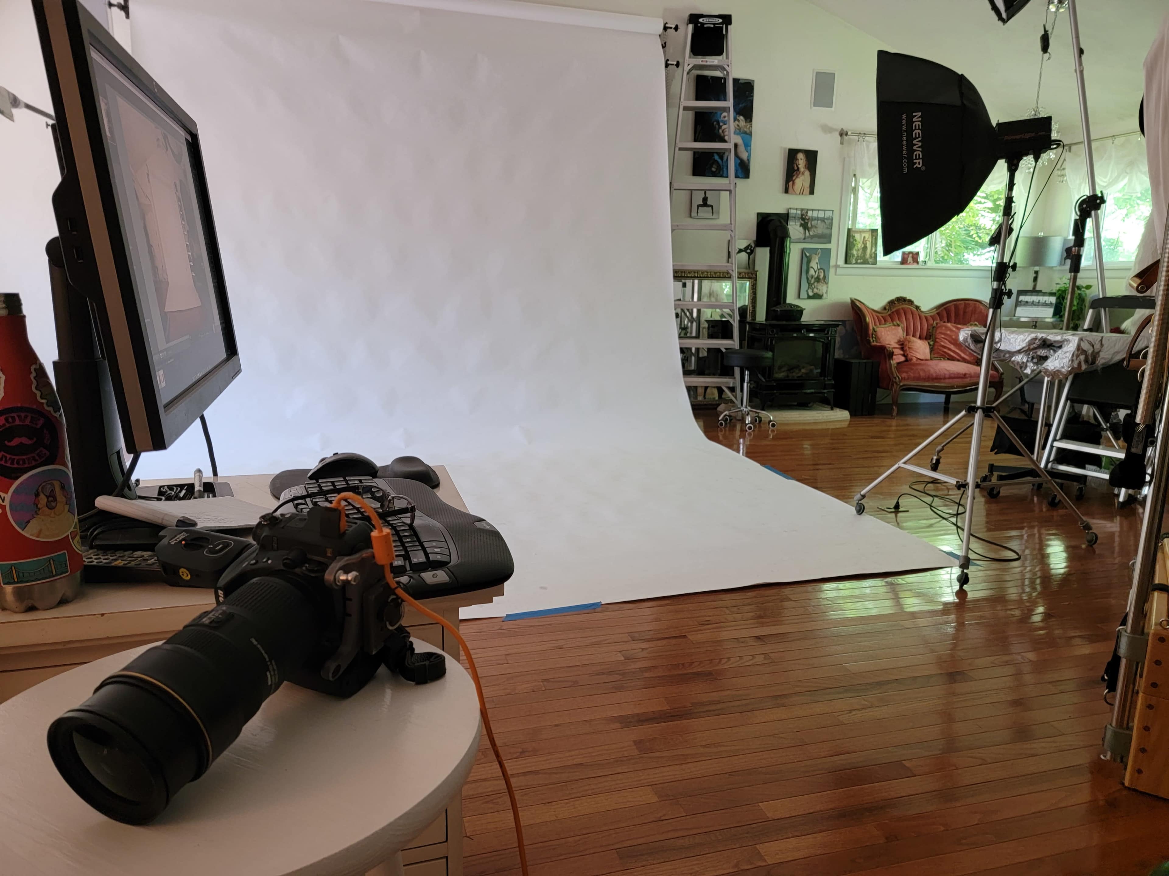 A photography studio setup includes a camera on a table, a backdrop, studio lights, and various props in the background.