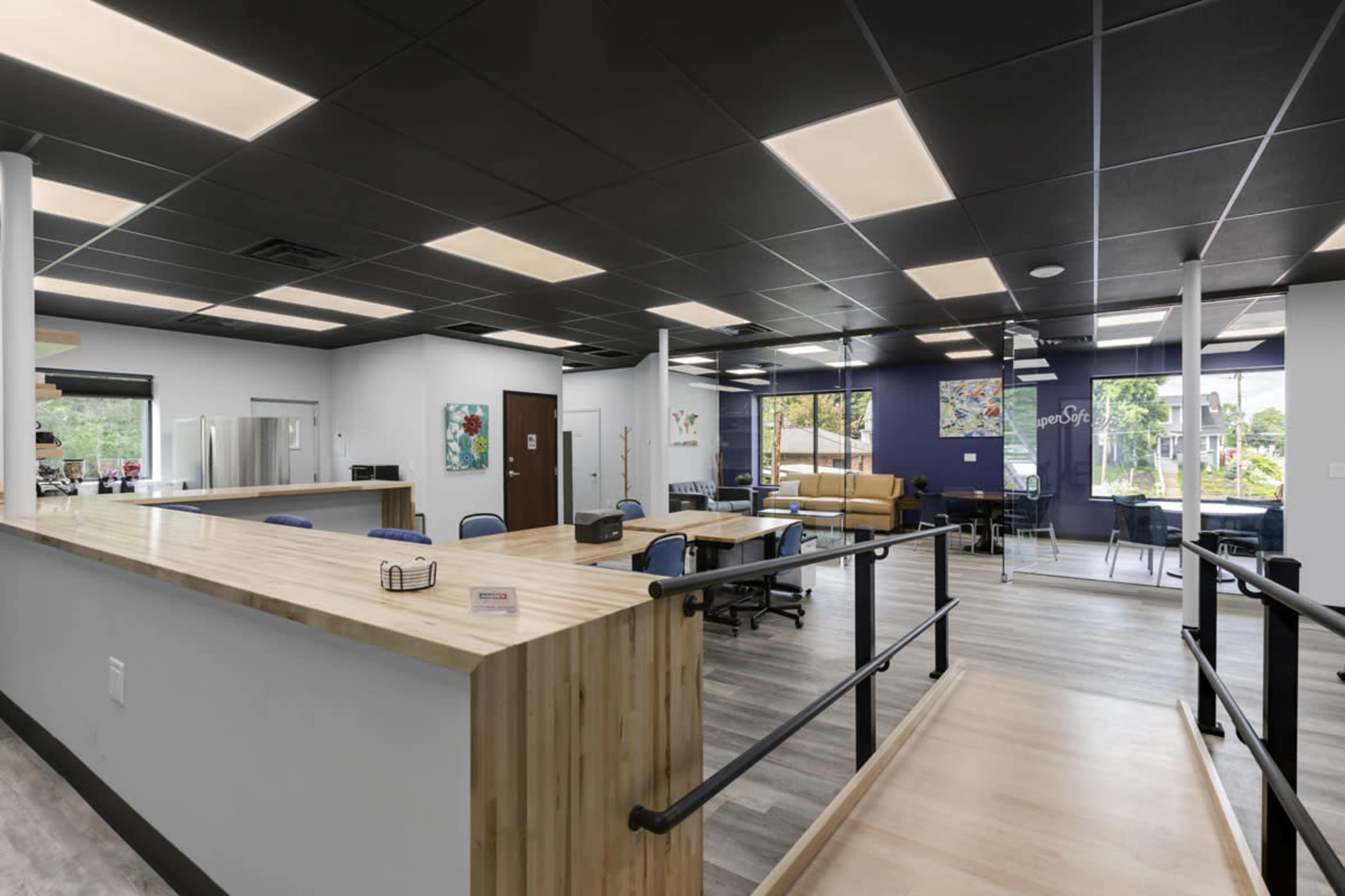 The image shows a modern office space with a wooden reception desk, seating areas, and artwork on the walls, all under bright ceiling lights.