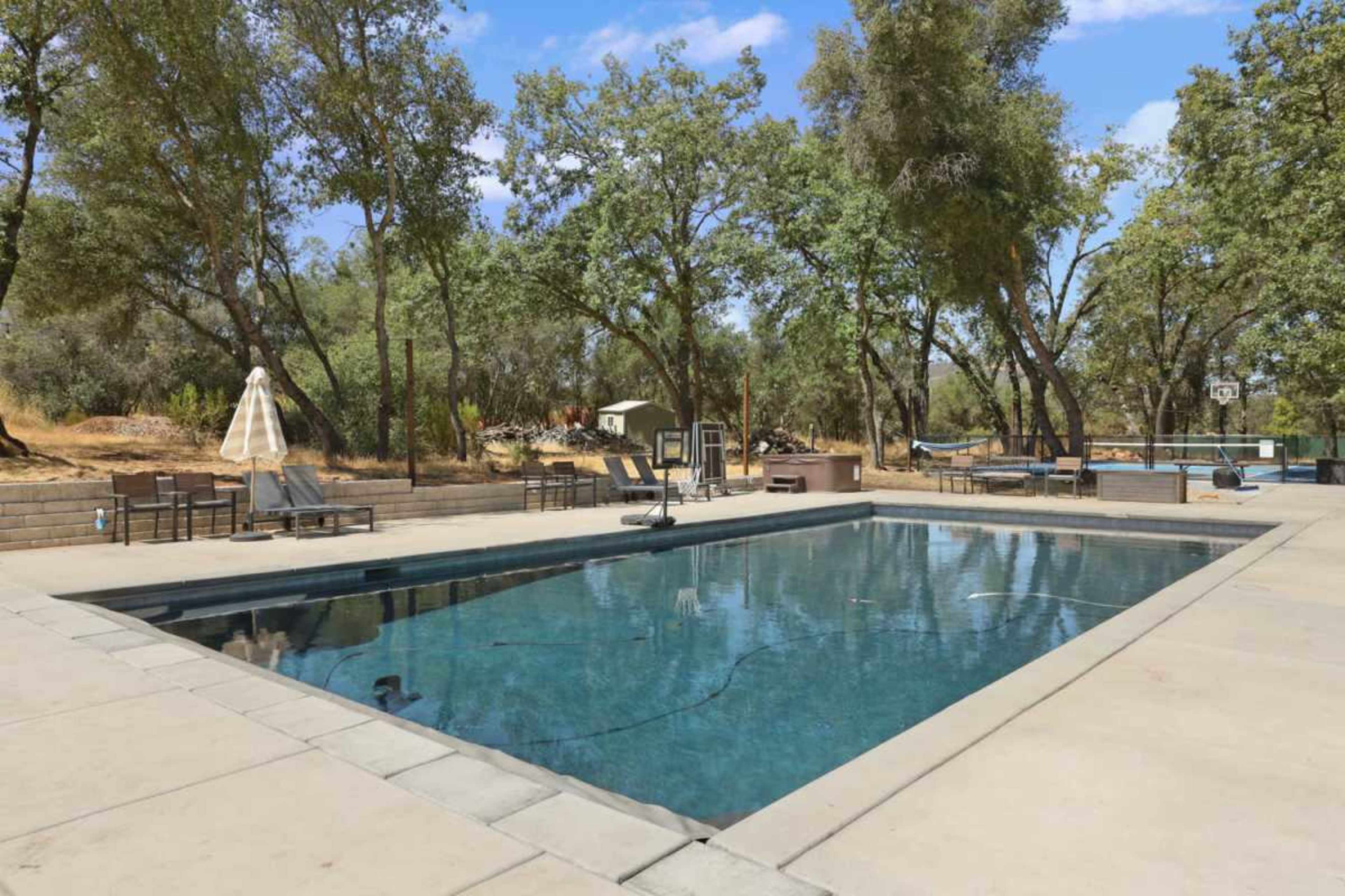 The image shows a rectangular swimming pool surrounded by lounge chairs and trees in a spacious outdoor area.