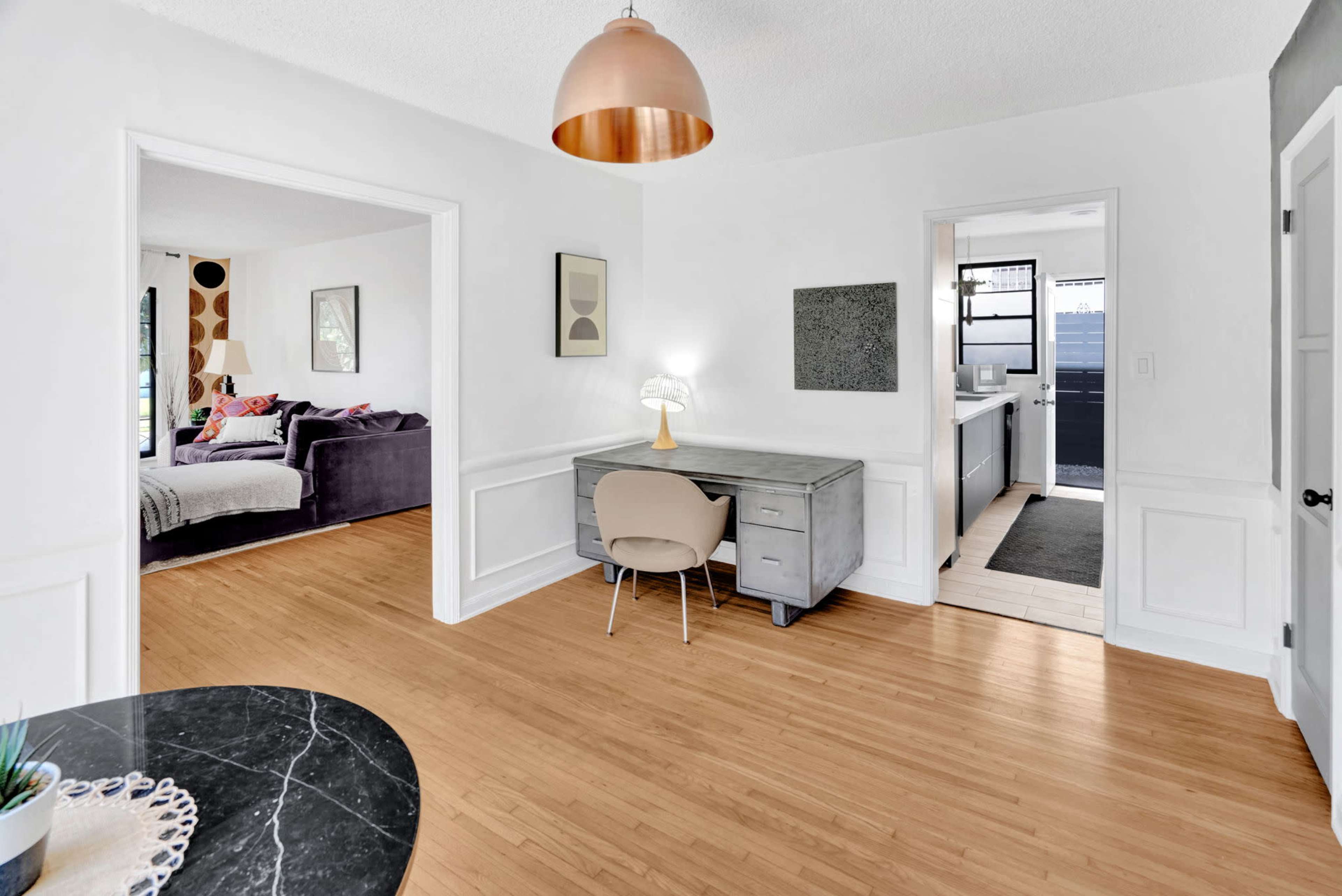A modern, open-concept living space features a desk area and leads to a kitchen with a view of a separate seating area.