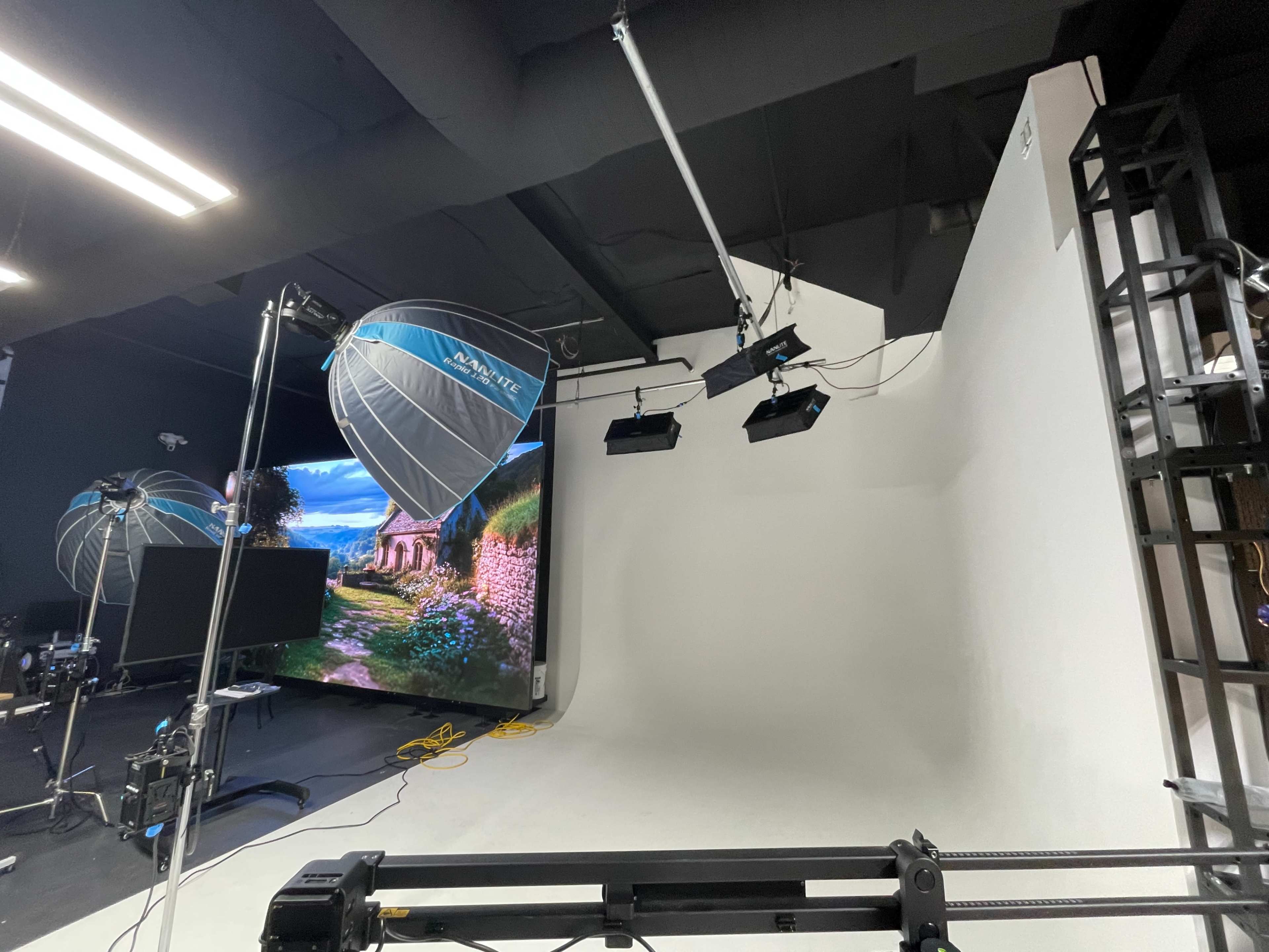The image shows a photography studio setup with softbox lights and a large backdrop displaying a scenic landscape.