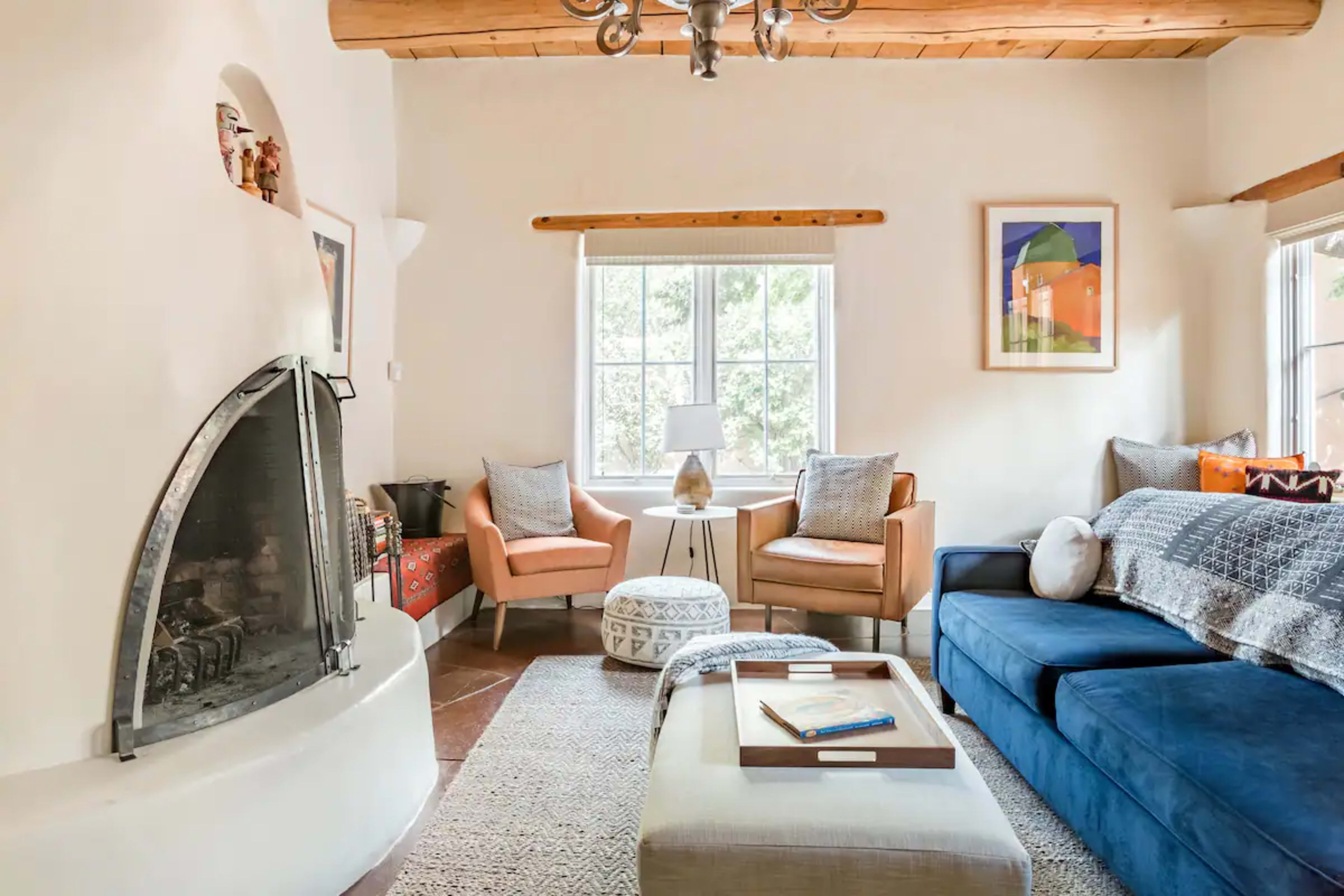 A cozy living room features a blue sofa, two seating chairs, a round ottoman, and a fireplace with a unique curved design.