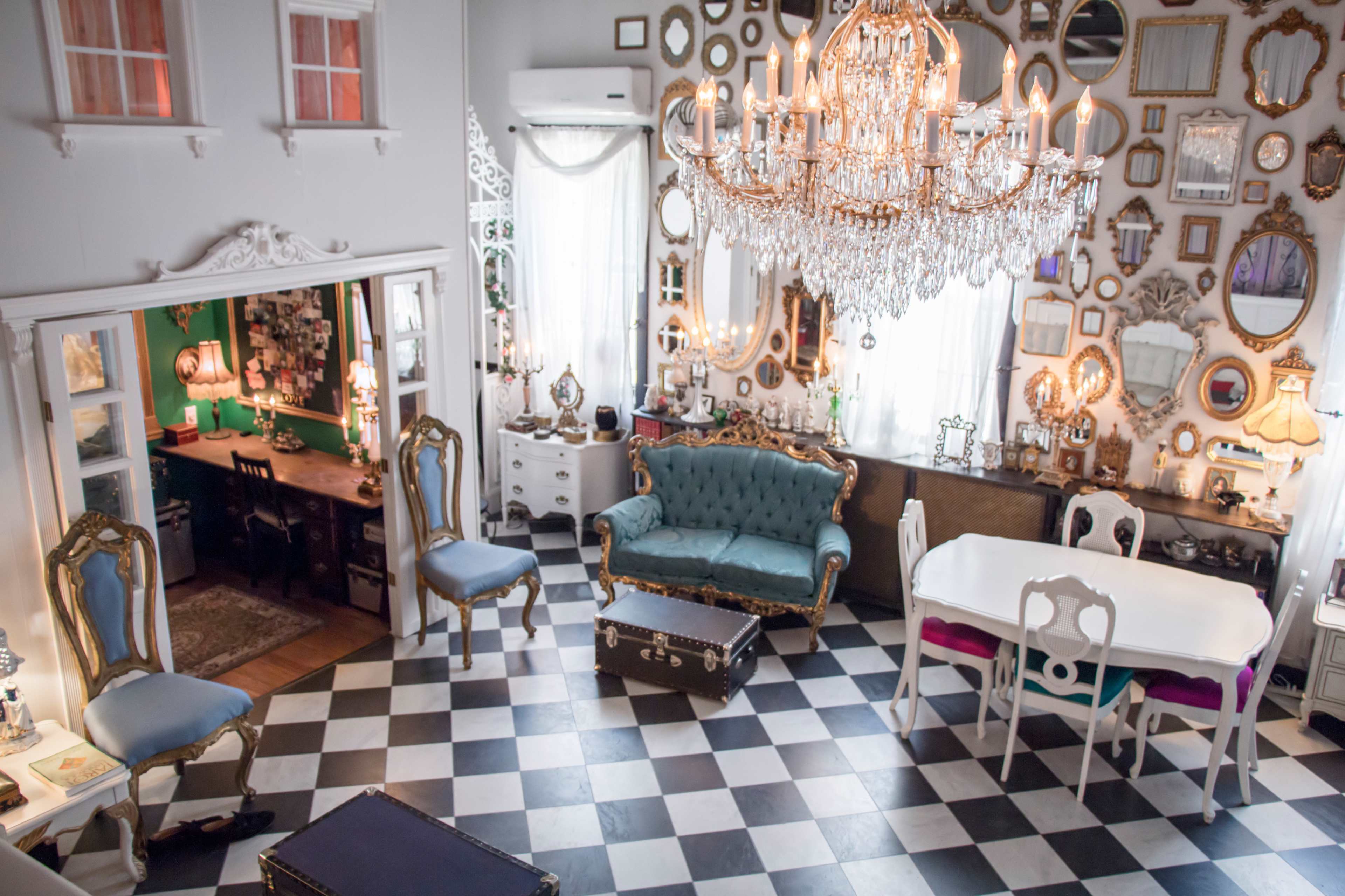 A stylishly decorated interior with a large chandelier, an assortment of mirrors on the wall, a turquoise couch, and a black-and-white checkered floor.