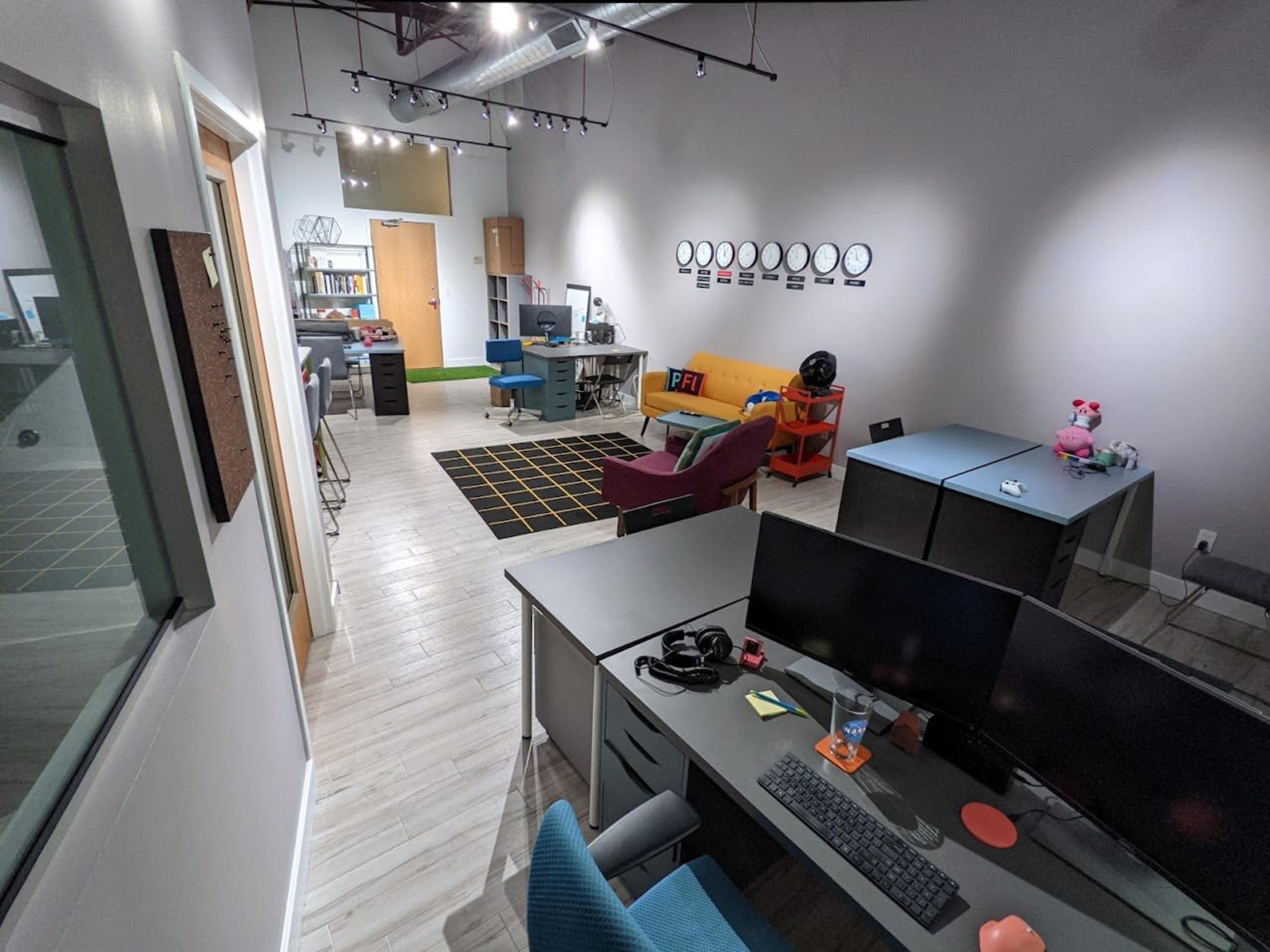 A modern office space with several workstations, a lounge area, and a wall featuring circular clock decorations.