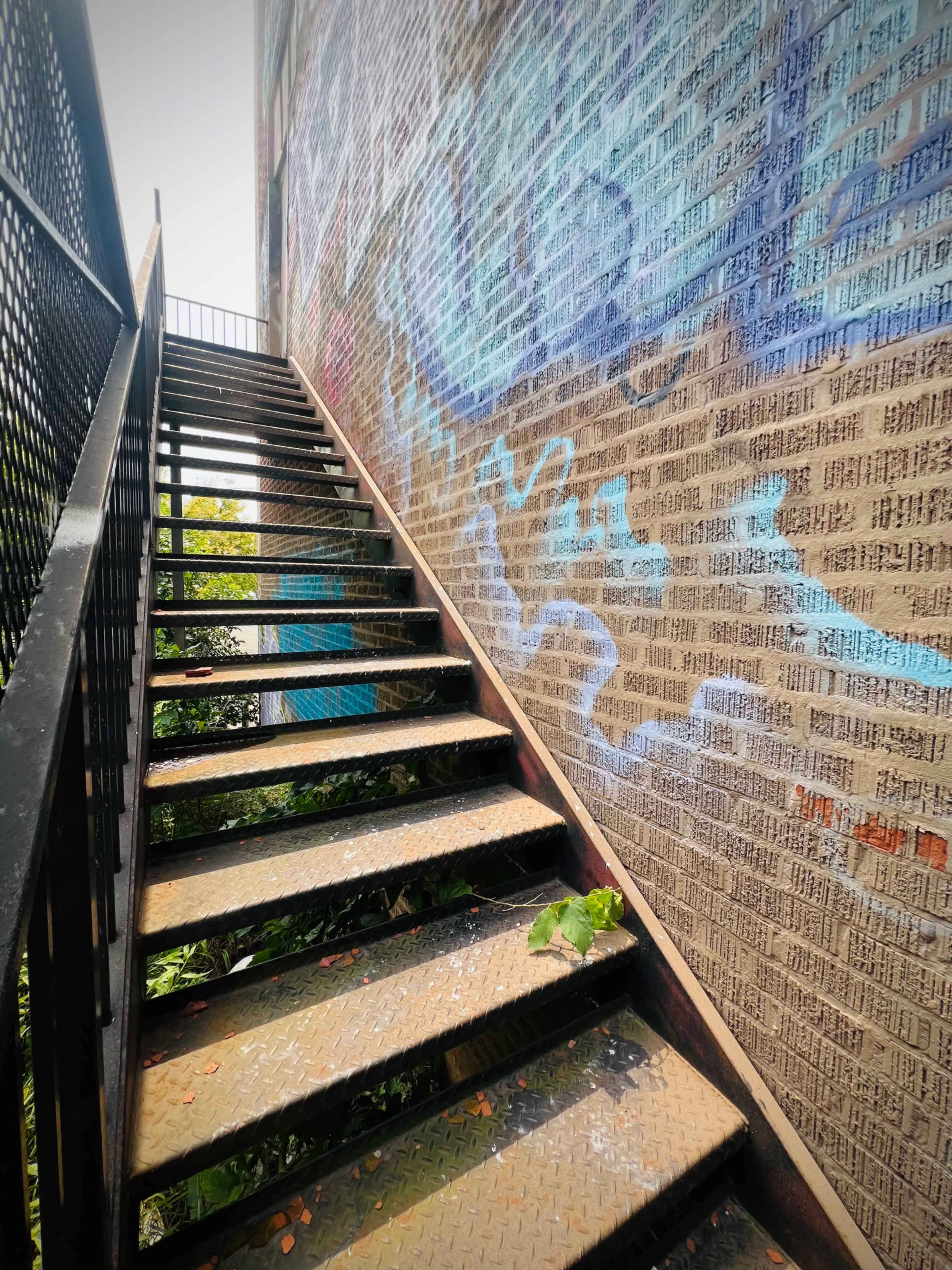 A metal staircase ascends alongside a brick wall adorned with colorful graffiti.