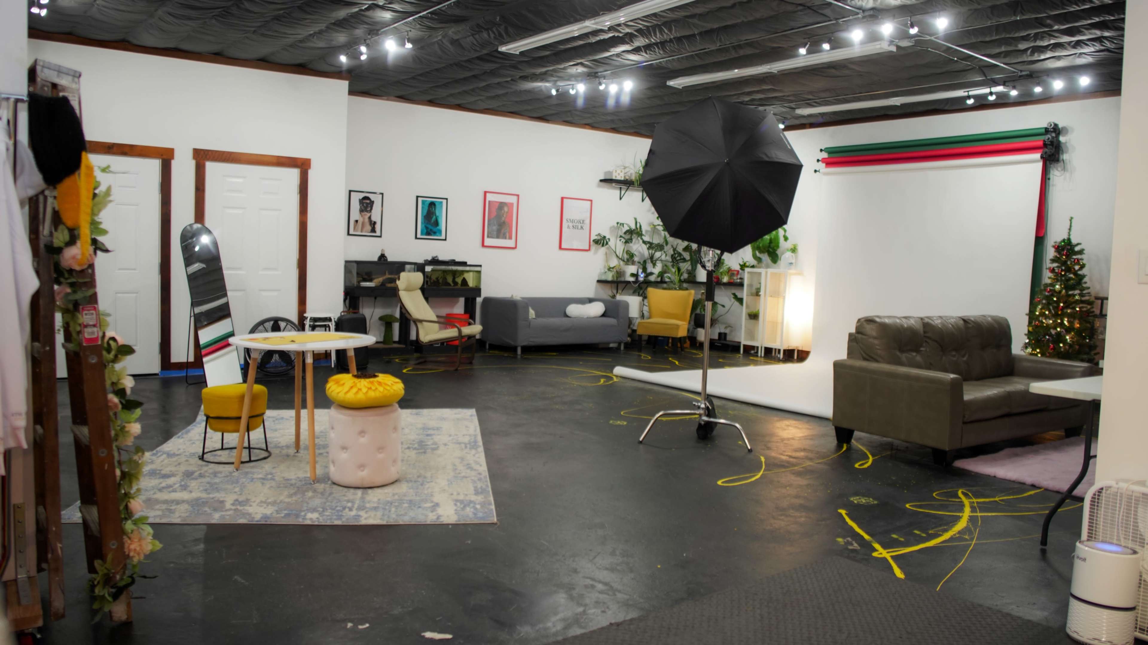 The image shows a spacious interior designed for a photo shoot, featuring various seating arrangements, decorative plants, and photography equipment.