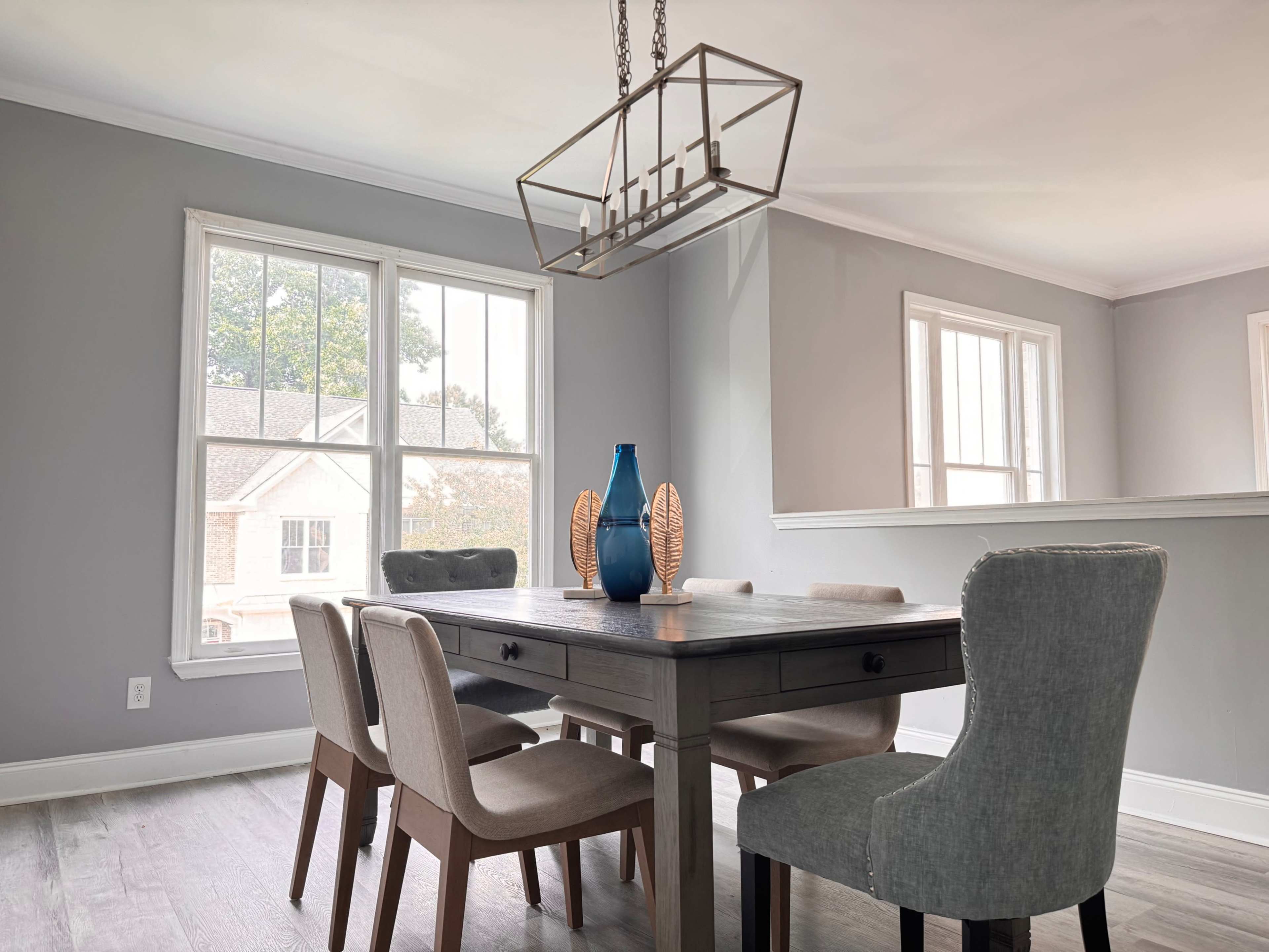 A dining room features a wooden table surrounded by upholstered chairs and a decorative vase on the table.
