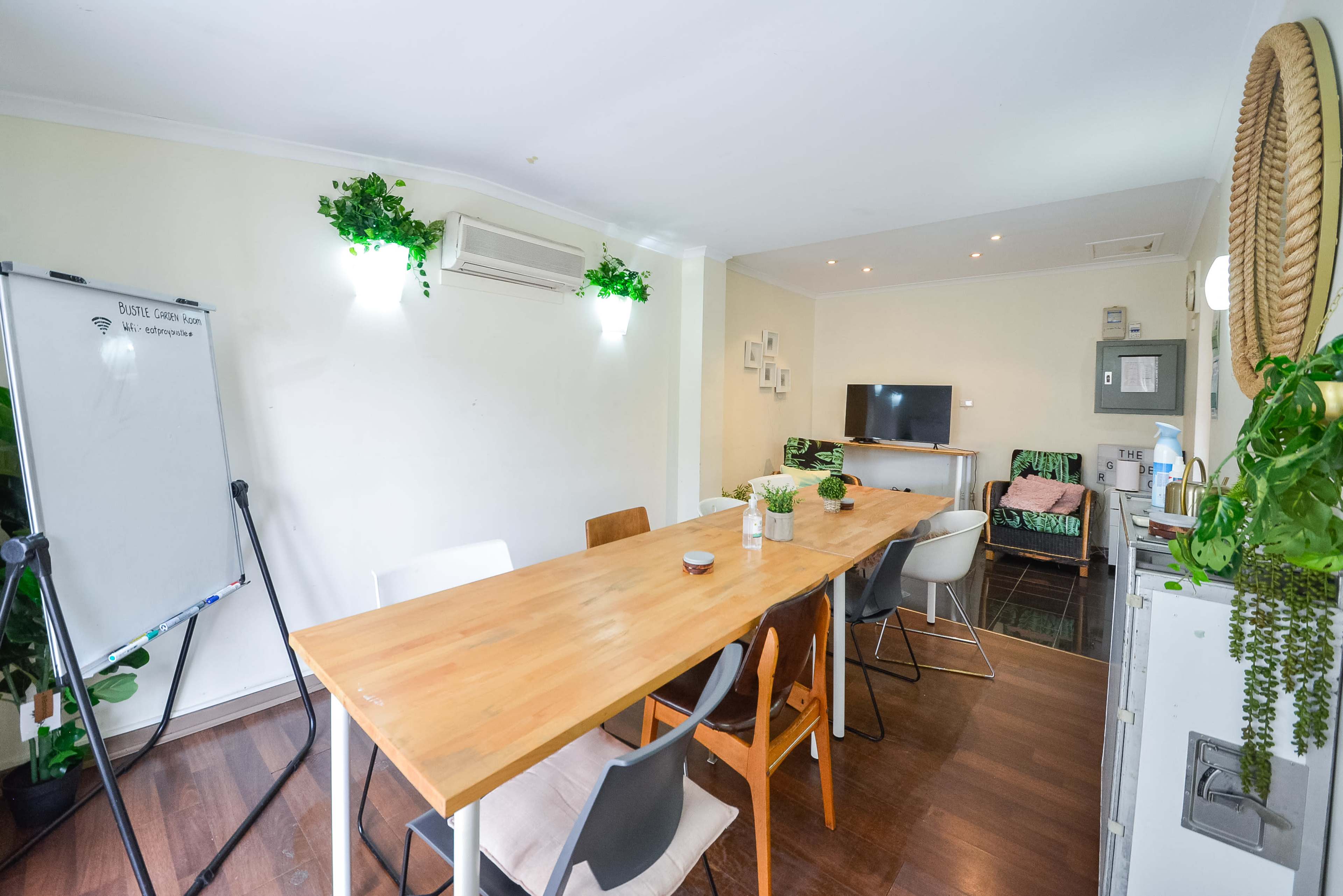 A bright, modern dining area featuring a wooden table with several chairs, a whiteboard, and a television on the wall.
