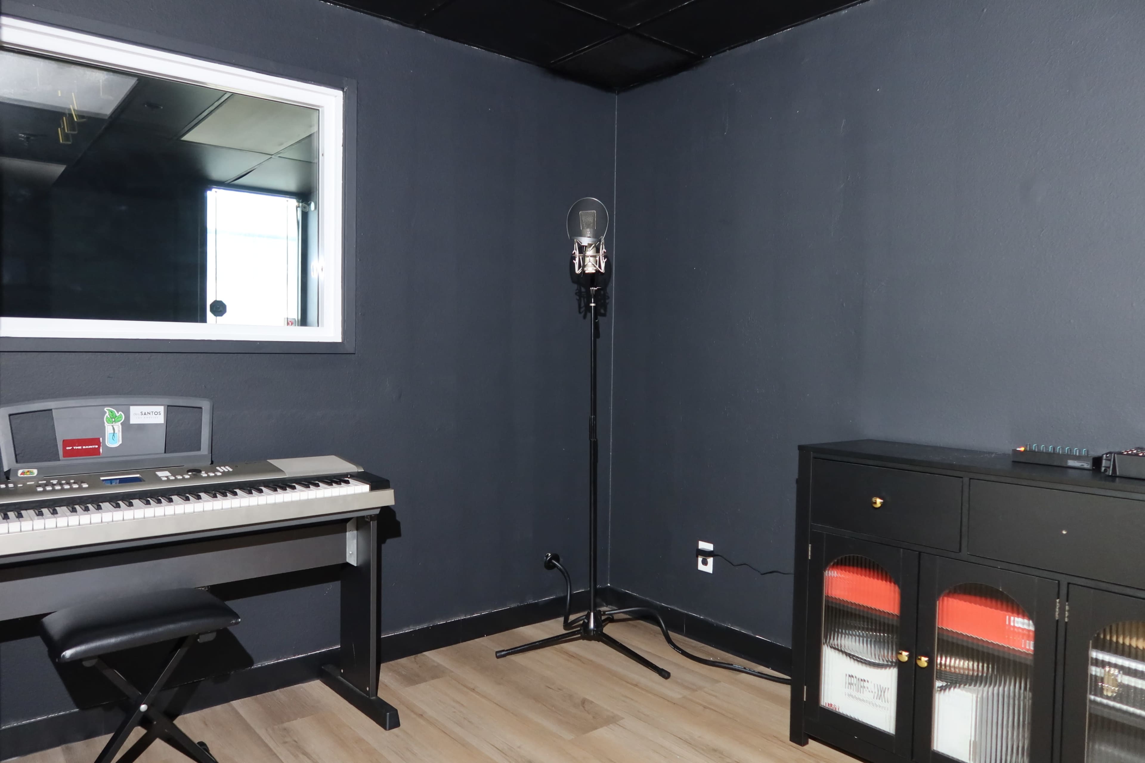 The image shows a recording studio with a keyboard, a microphone stand, and a cabinet against dark walls.