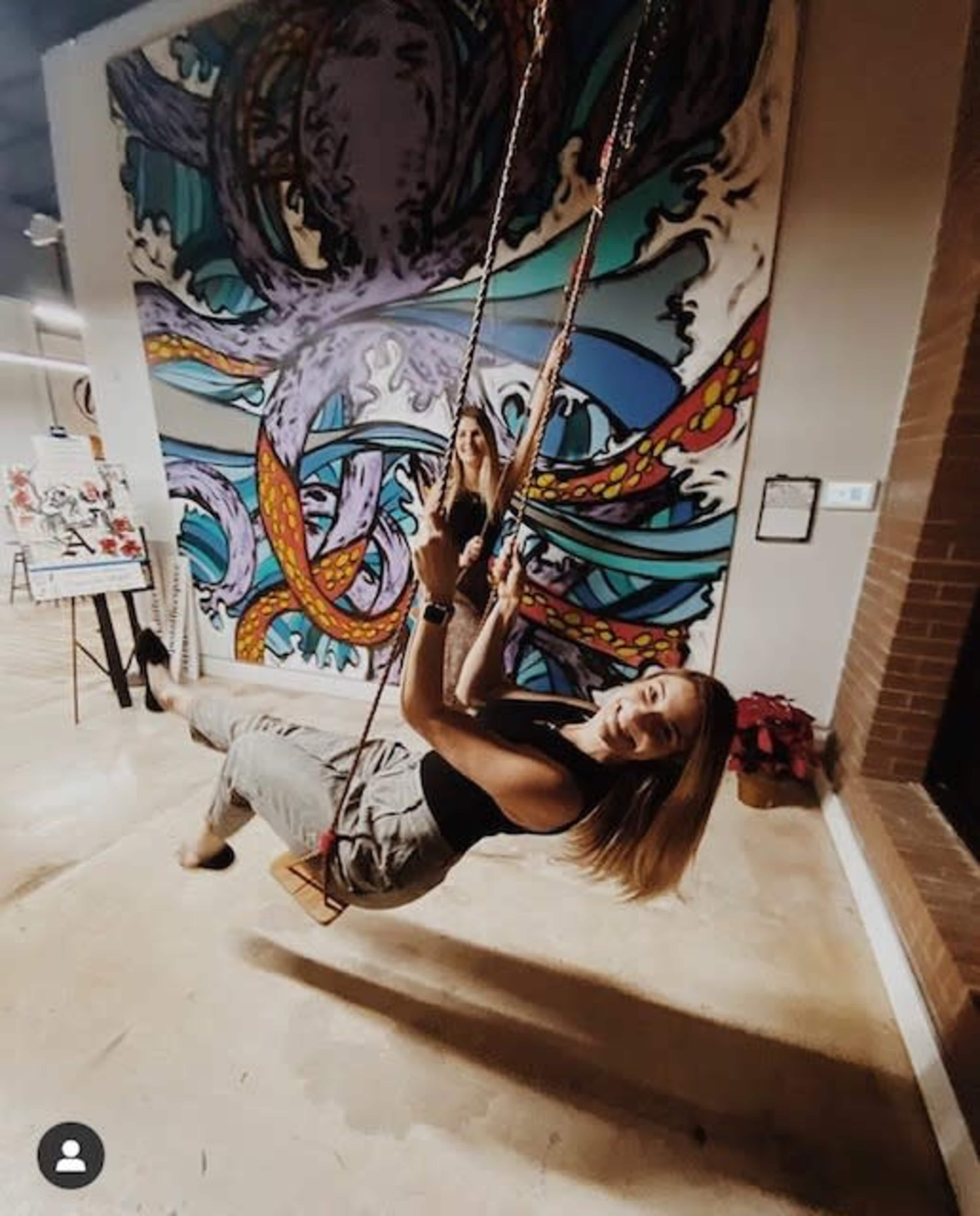 A woman swings on a rope swing in front of a colorful mural depicting an octopus.