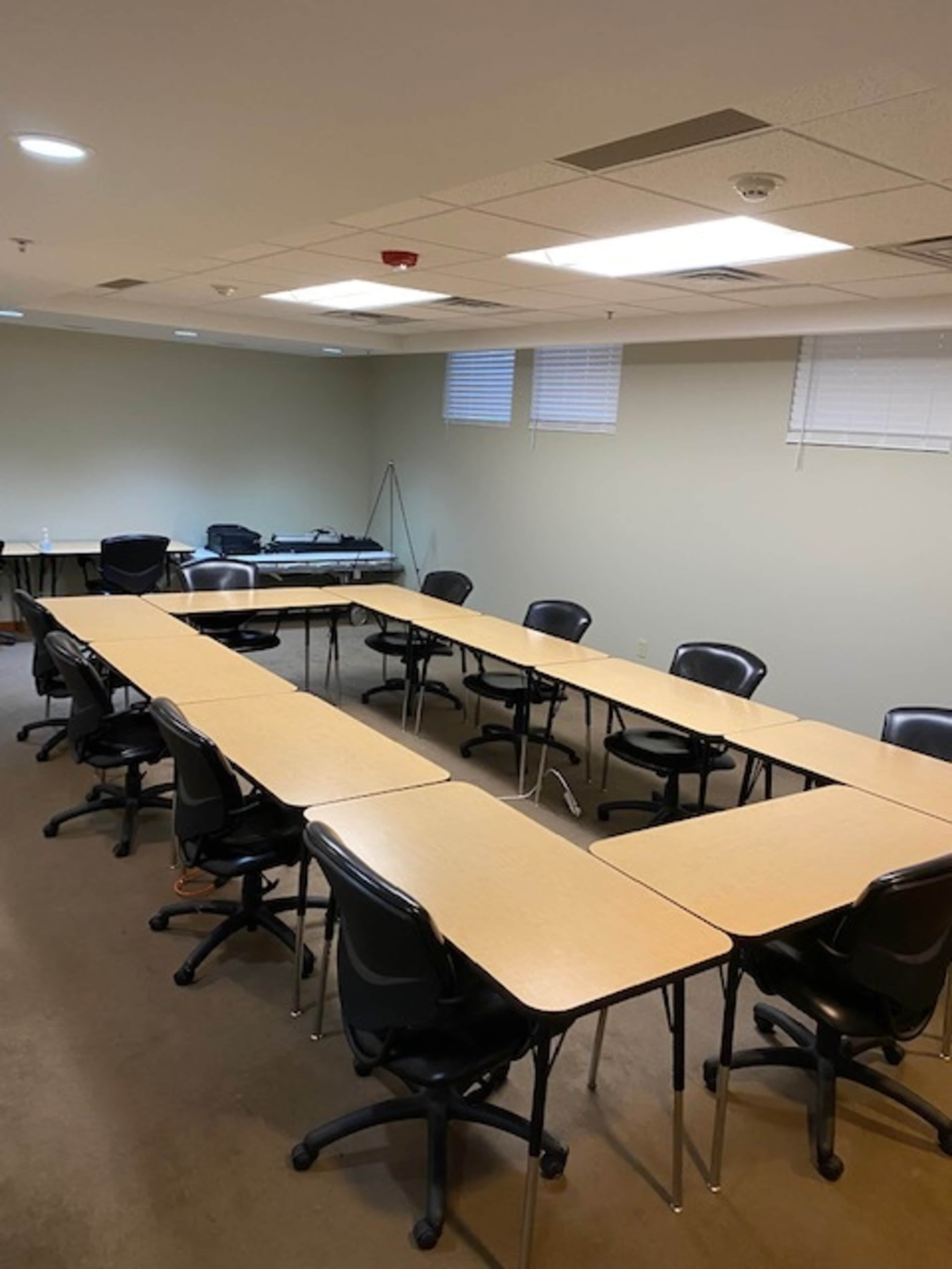 A rectangular meeting room with multiple tables arranged in a U-shape and black chairs placed around them.