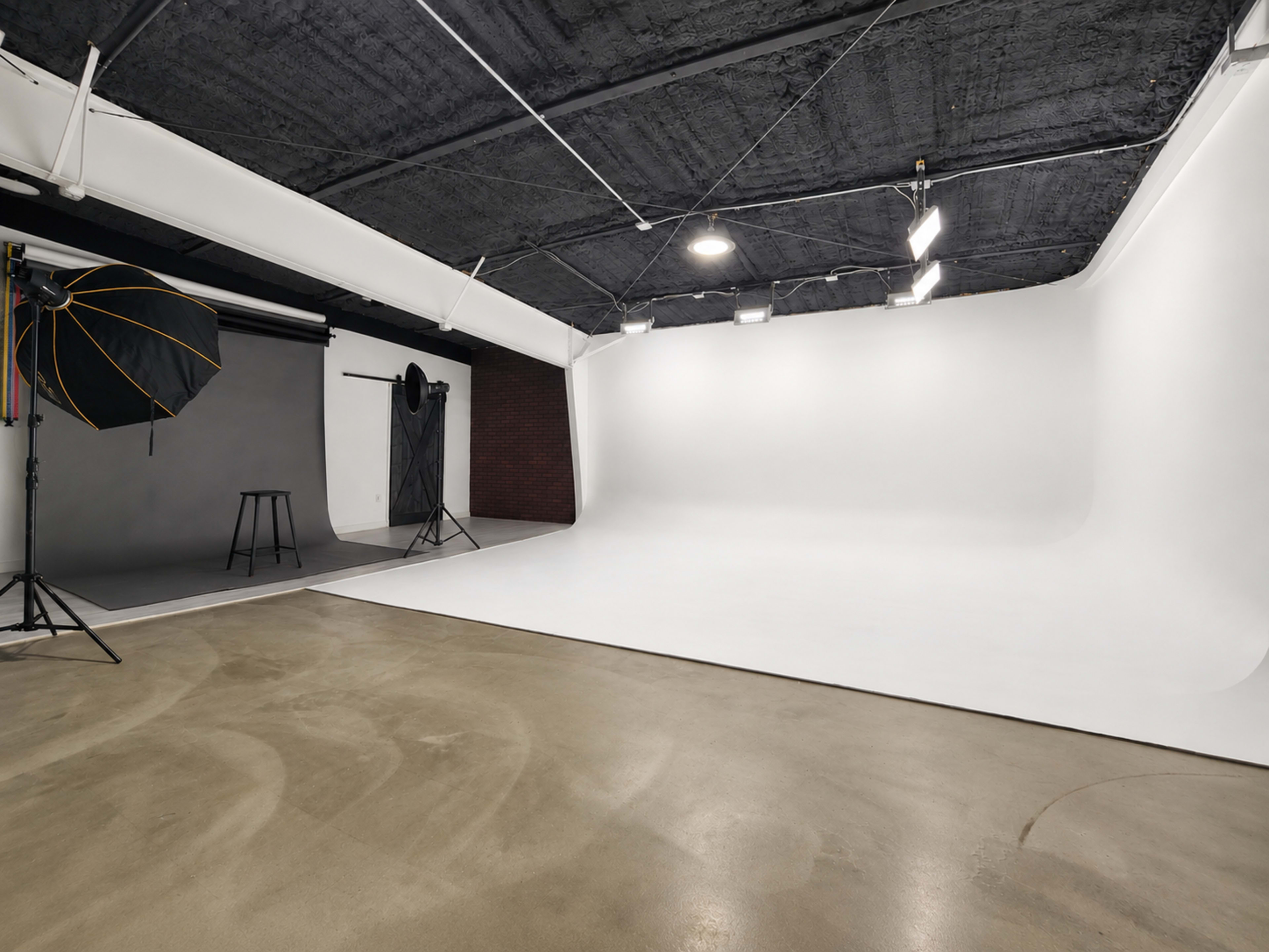 The image shows a photography studio with a large white backdrop, lighting equipment, and a seamless floor.