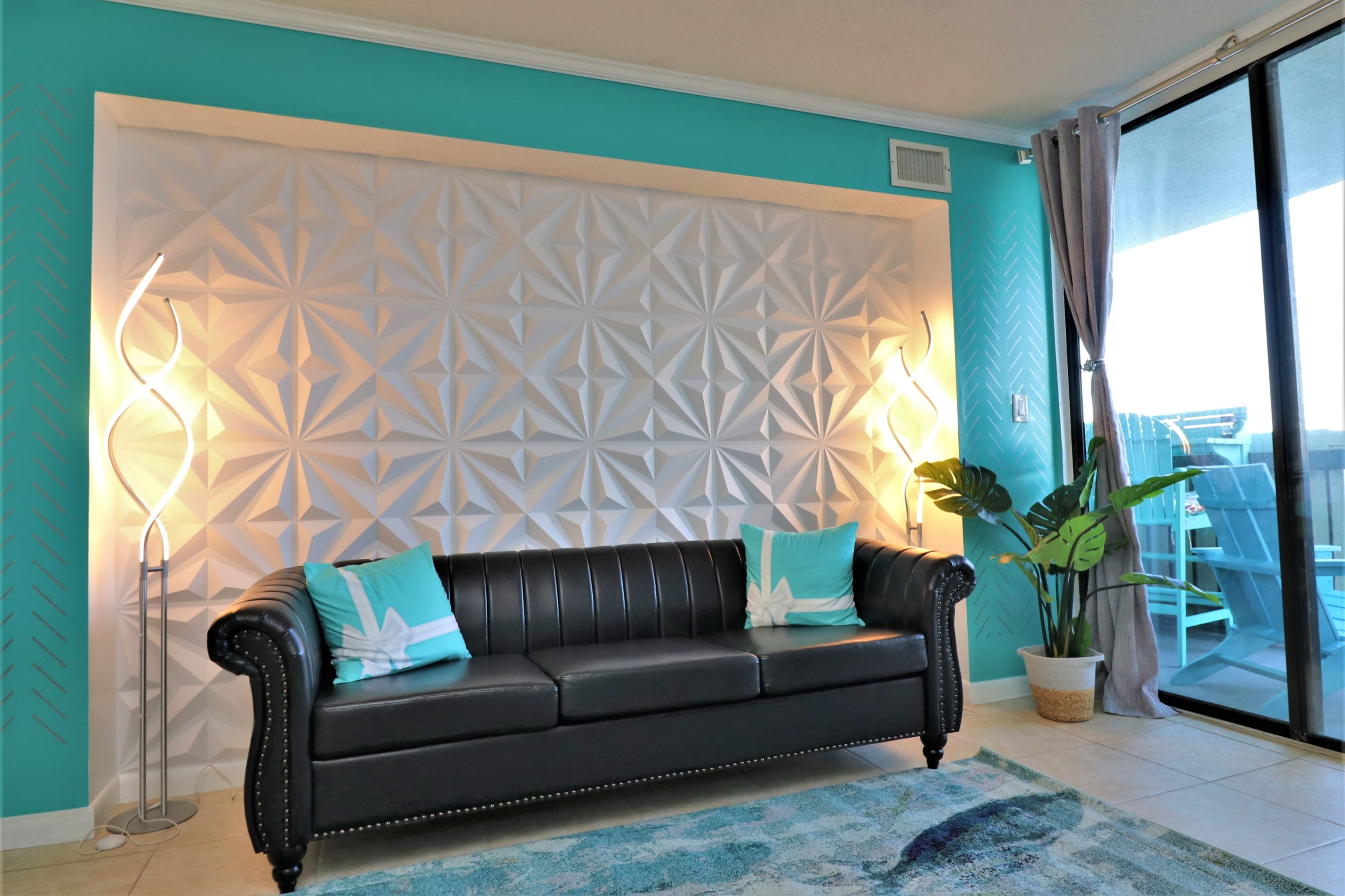A modern living room featuring a black leather sofa with teal accents, a textured white wall, and two floor lamps on either side.