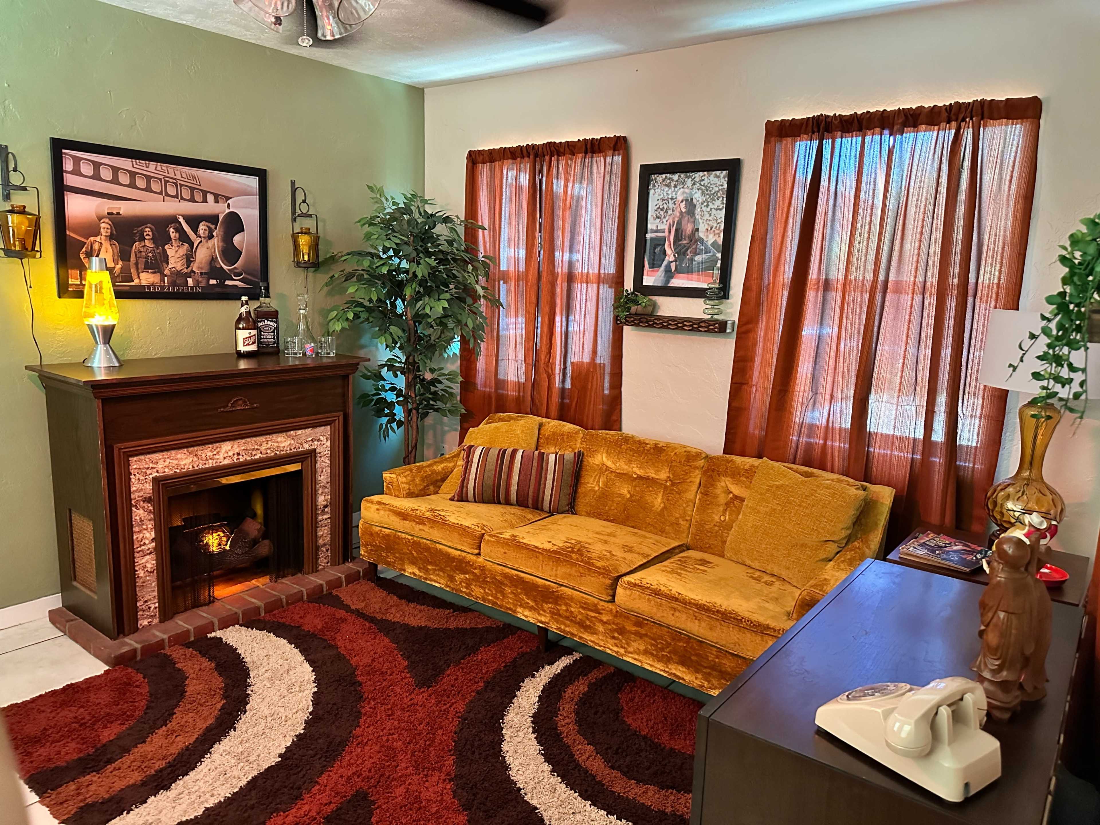 A cozy living room featuring a yellow velvet sofa, a decorative fireplace, and warm brown curtains.