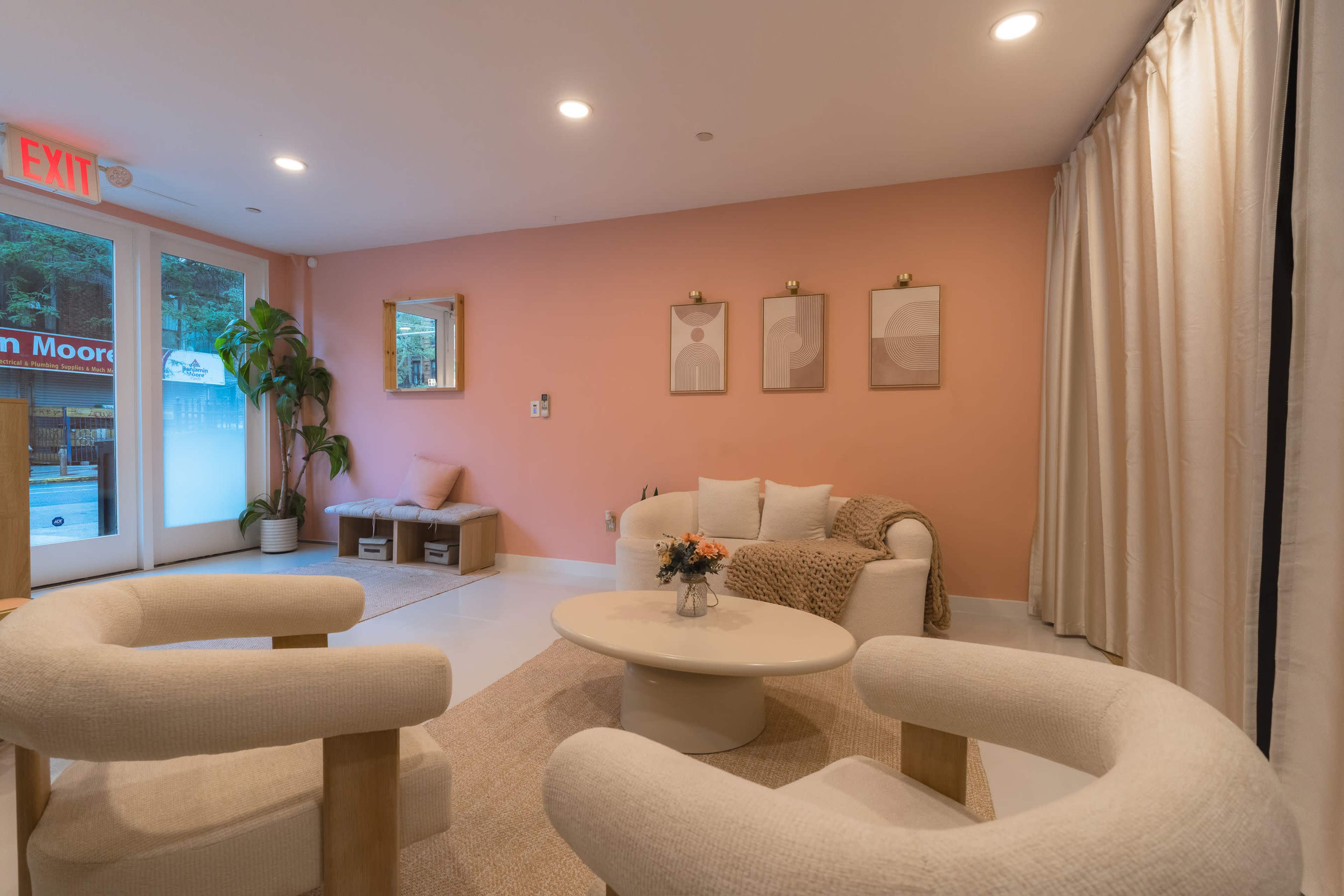 The image shows a cozy lounge area with two upholstered chairs, a round coffee table, and framed artwork on a peach-colored wall.