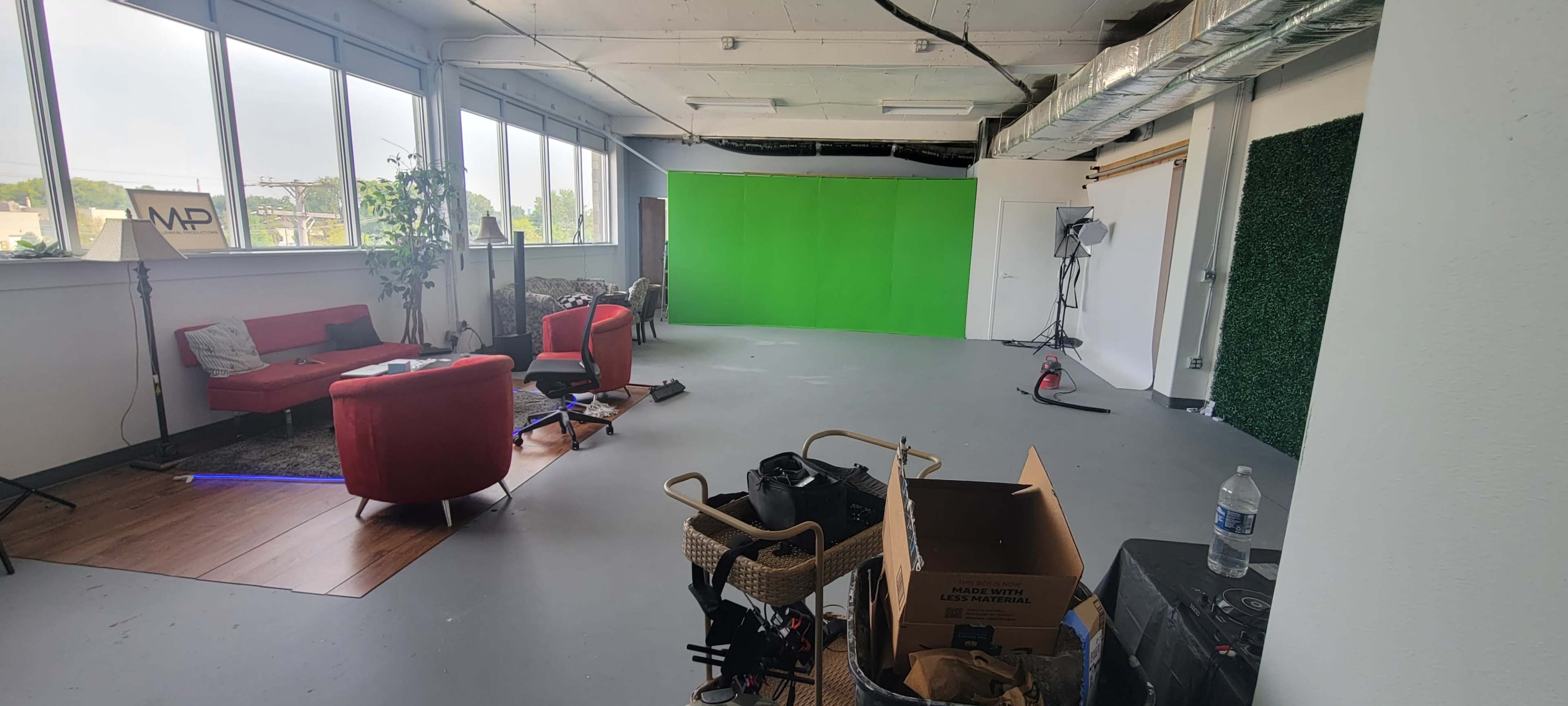 A spacious studio with green and white backdrops, red seating, various equipment, and large windows.