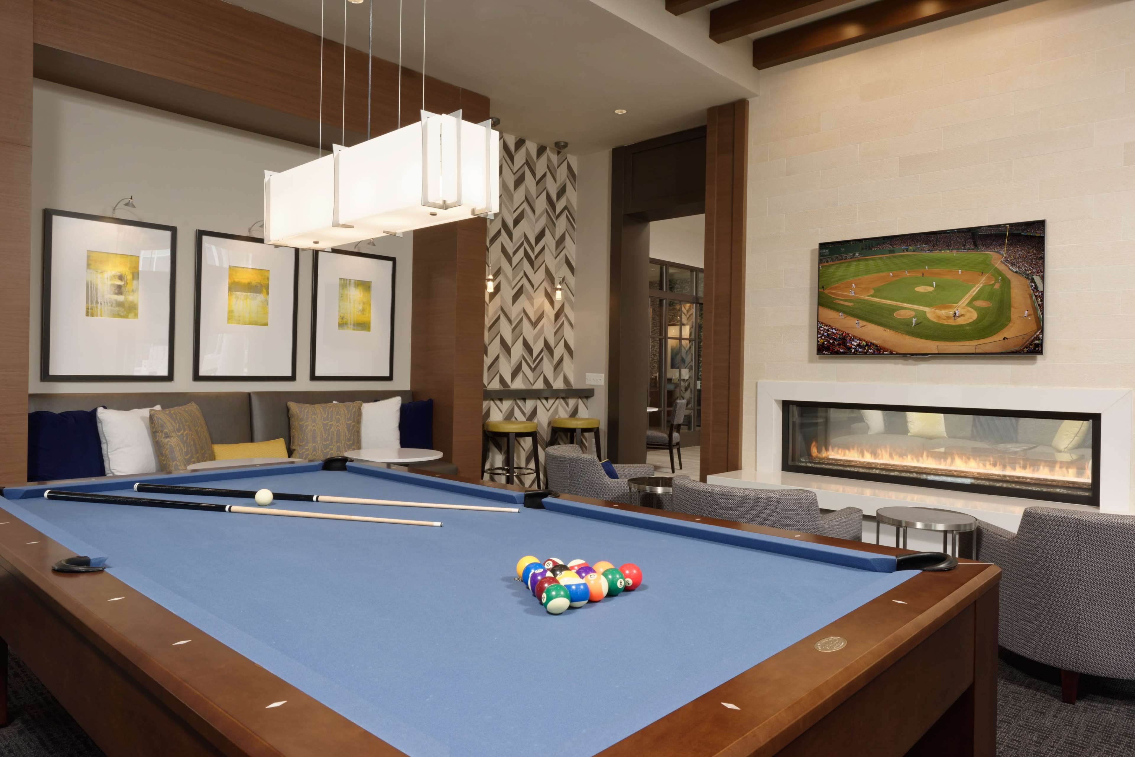 A modern recreational room featuring a blue pool table with balls arranged at one end, a gas fireplace, and a wall-mounted television displaying a sports scene.