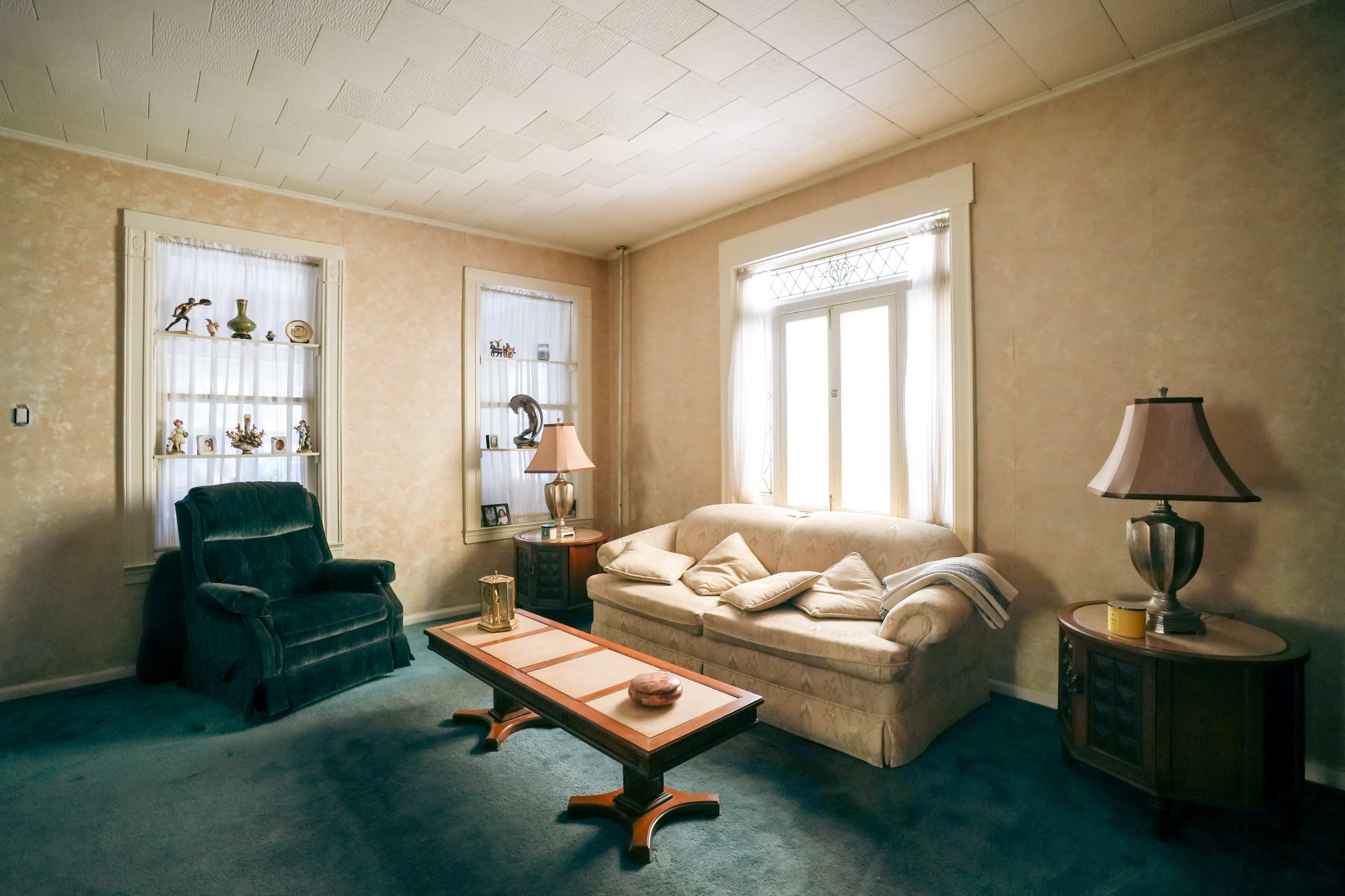 A living room features a plush sofa, an armchair, a coffee table, and shelves with decorative items against a pastel-painted wall.
