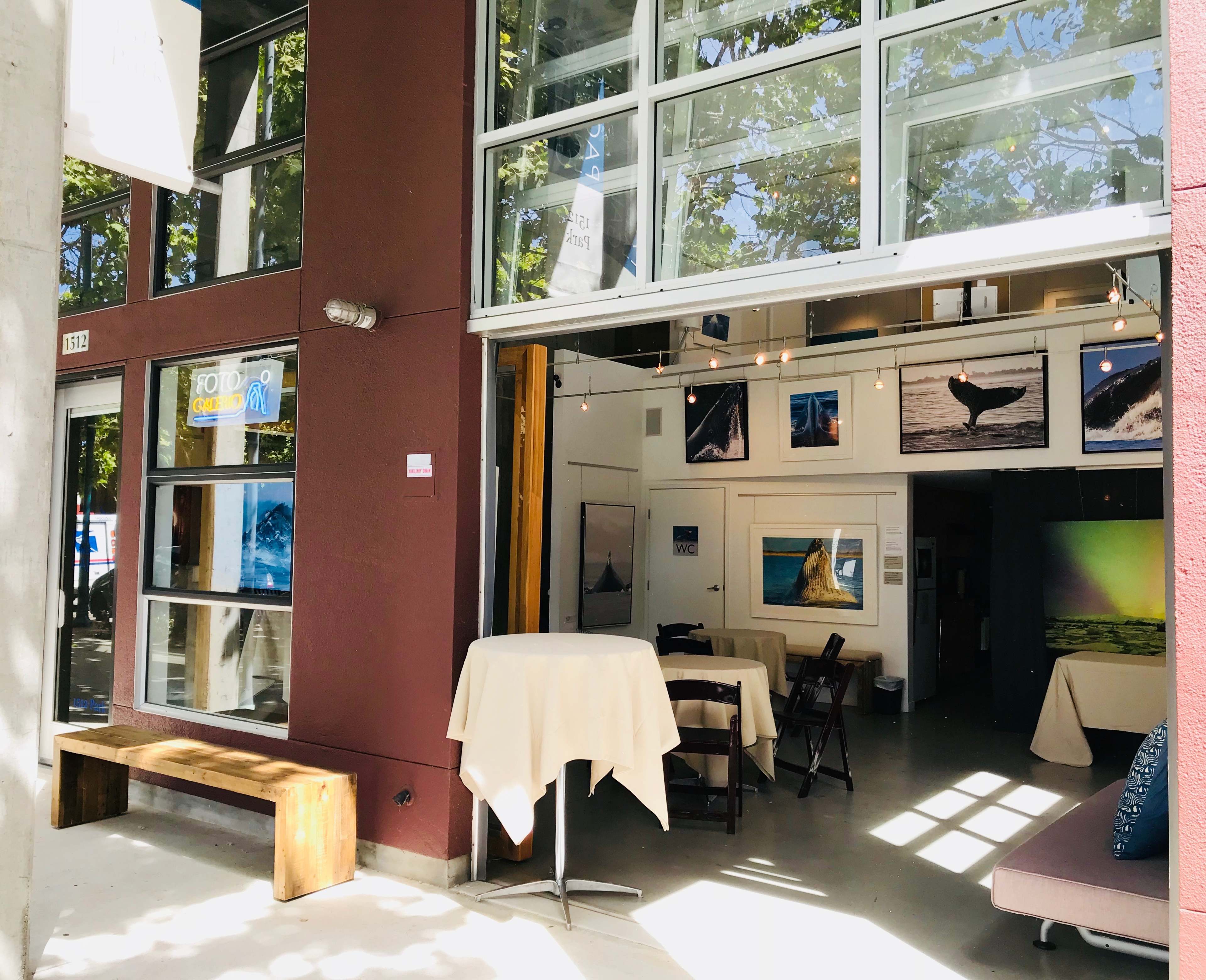 An open entrance to an art gallery or restaurant with wooden tables and photographs displayed on the walls.
