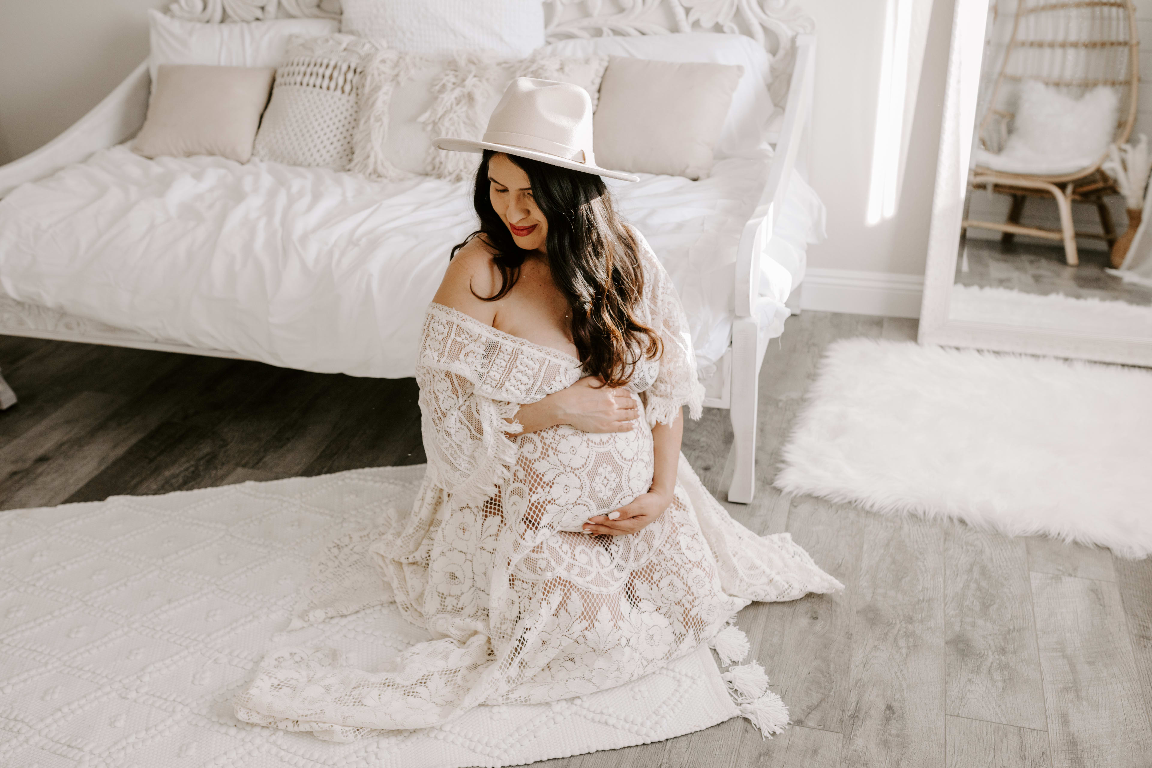 A woman in a boho white dress posing for a maternity photoshoot.