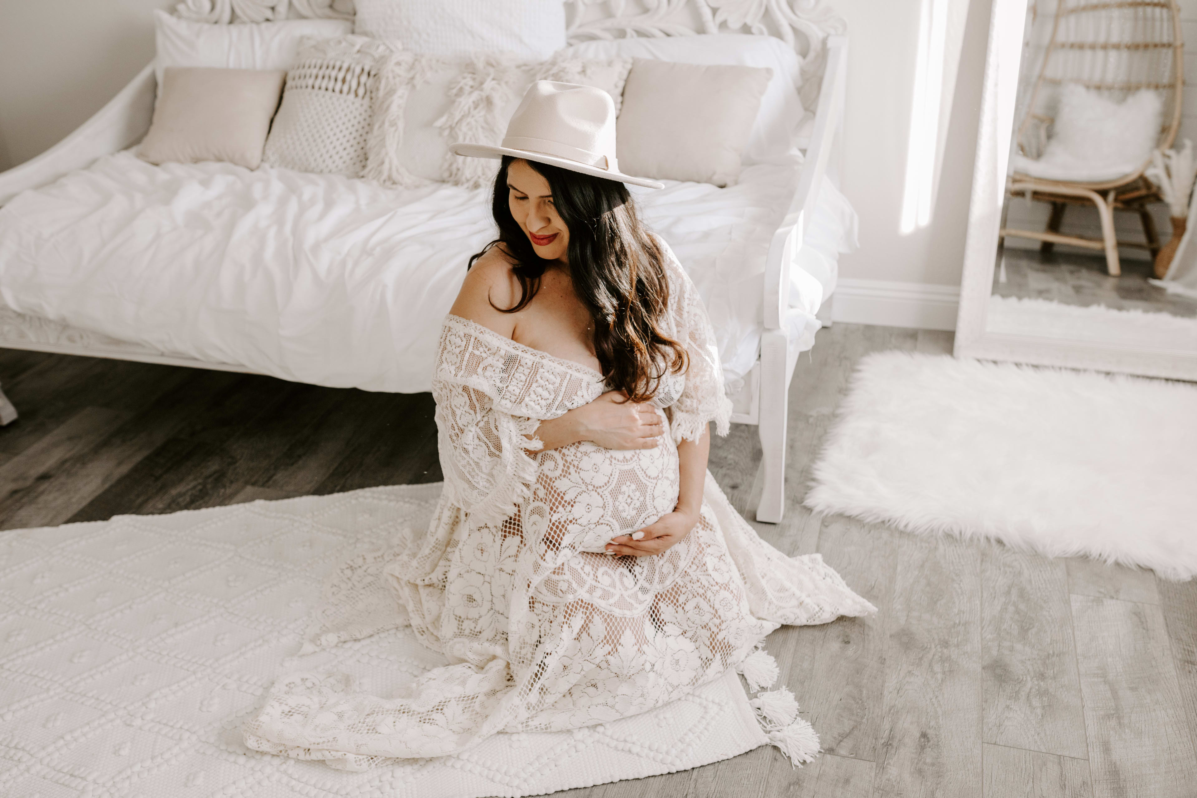 Una mujer con un vestido blanco boho posando para una sesión de fotos de maternidad.