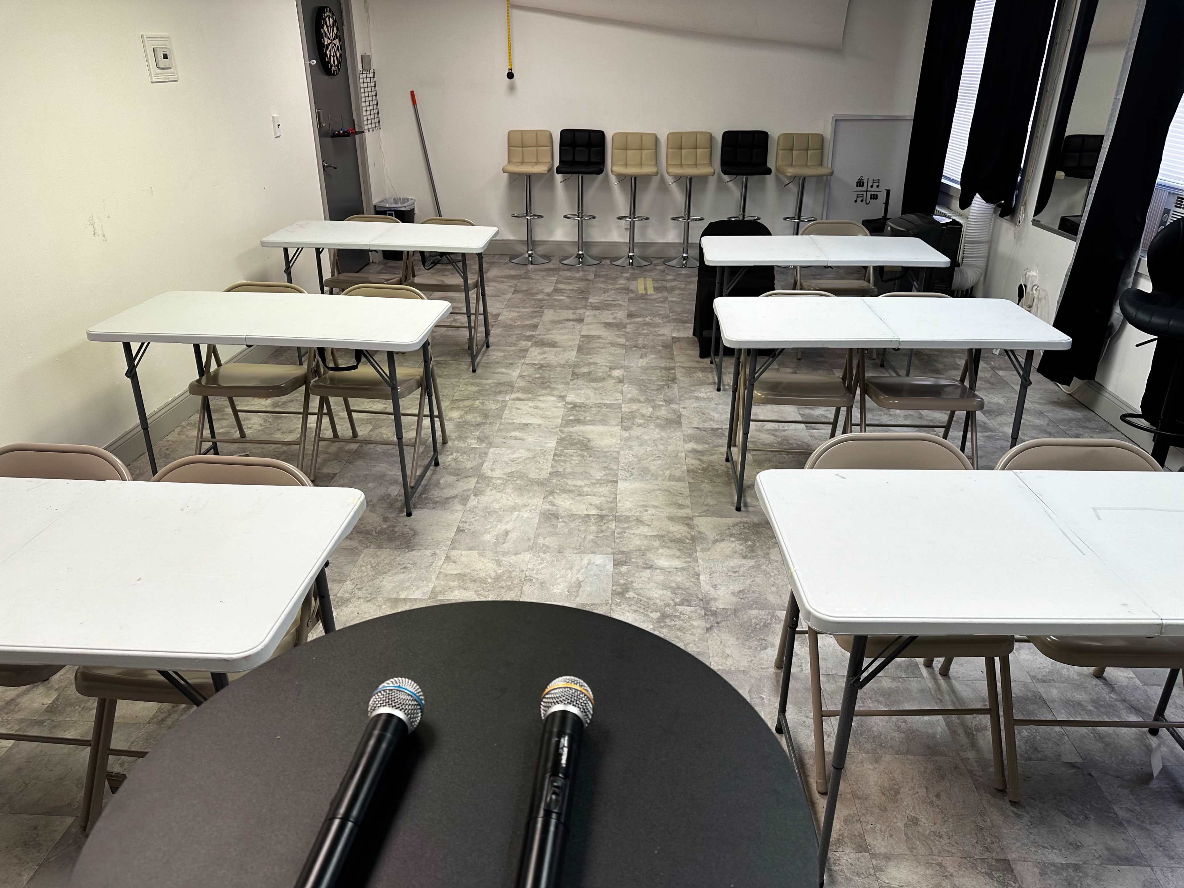 A room with several folding tables and chairs arranged in a grid layout, featuring two microphones in the foreground.