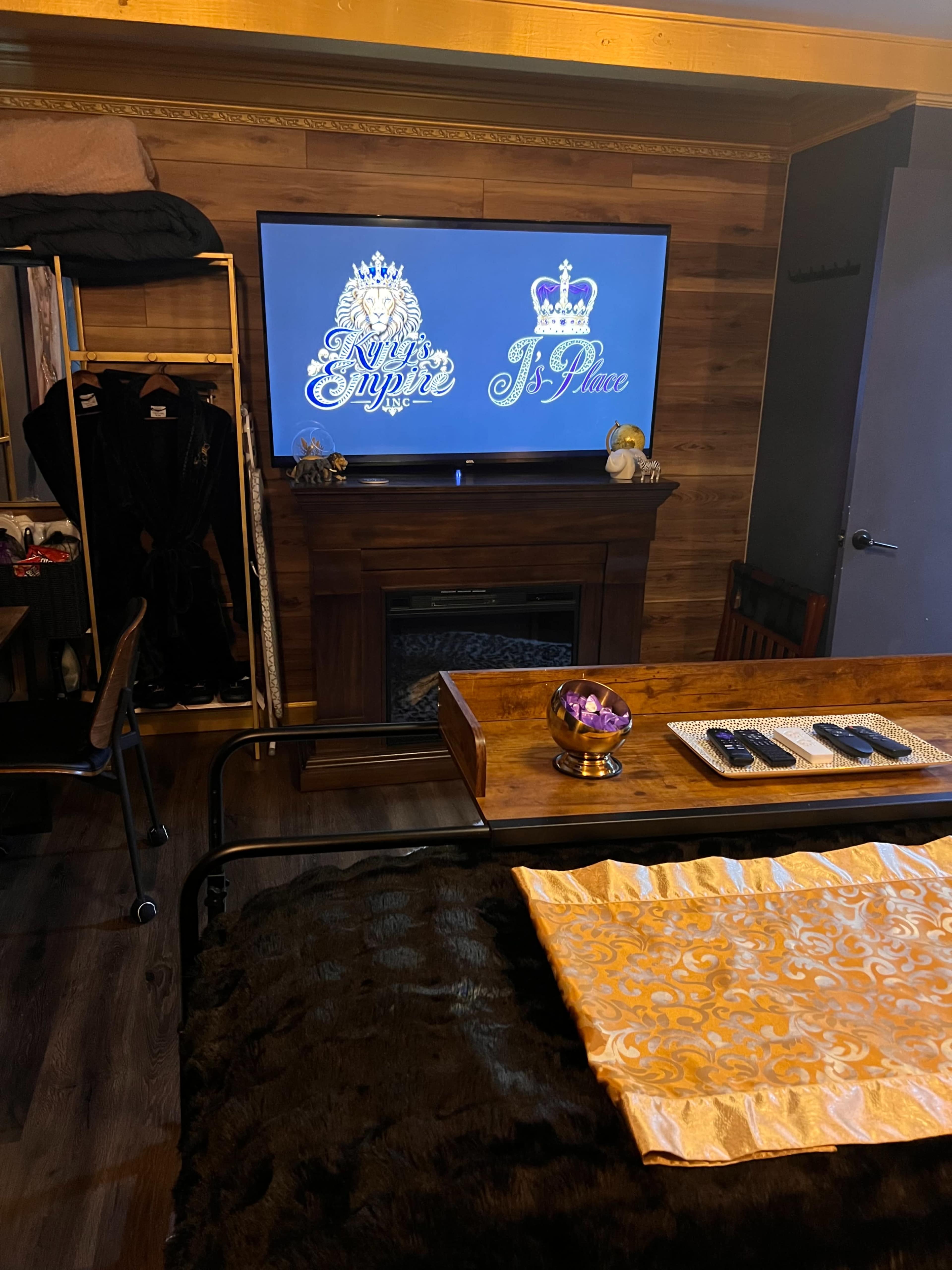 The image shows a room with a large television displaying two logos, a fireplace below it, and a table with decorative items in front.