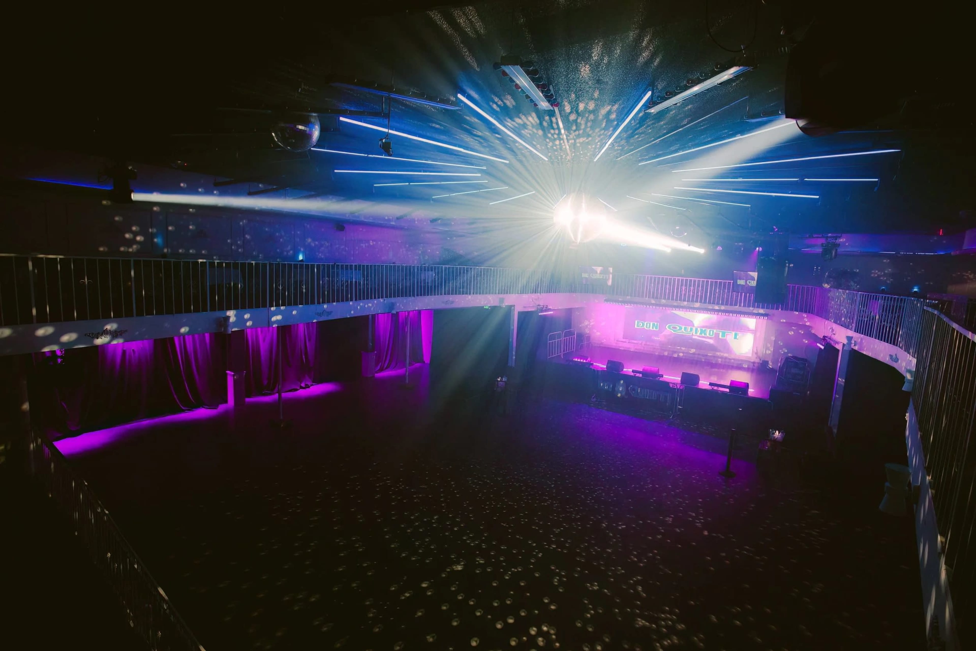 A spacious nightclub features a central stage with colorful lighting and a disco ball, surrounded by elevated seating areas.