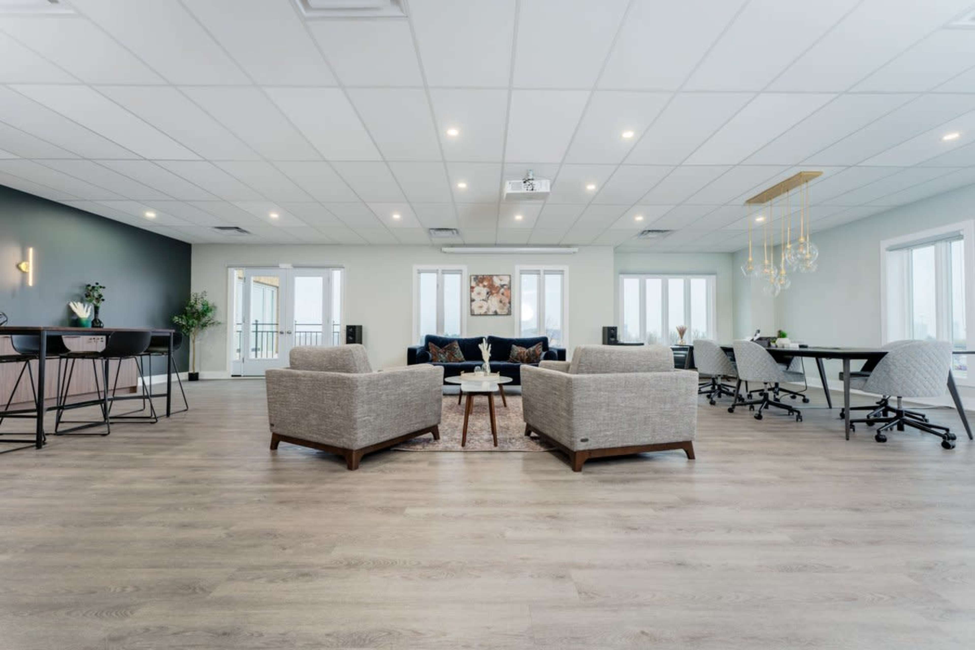 A modern office space featuring two upholstered chairs, a coffee table, and workstations arranged around a large, open area with natural light.
