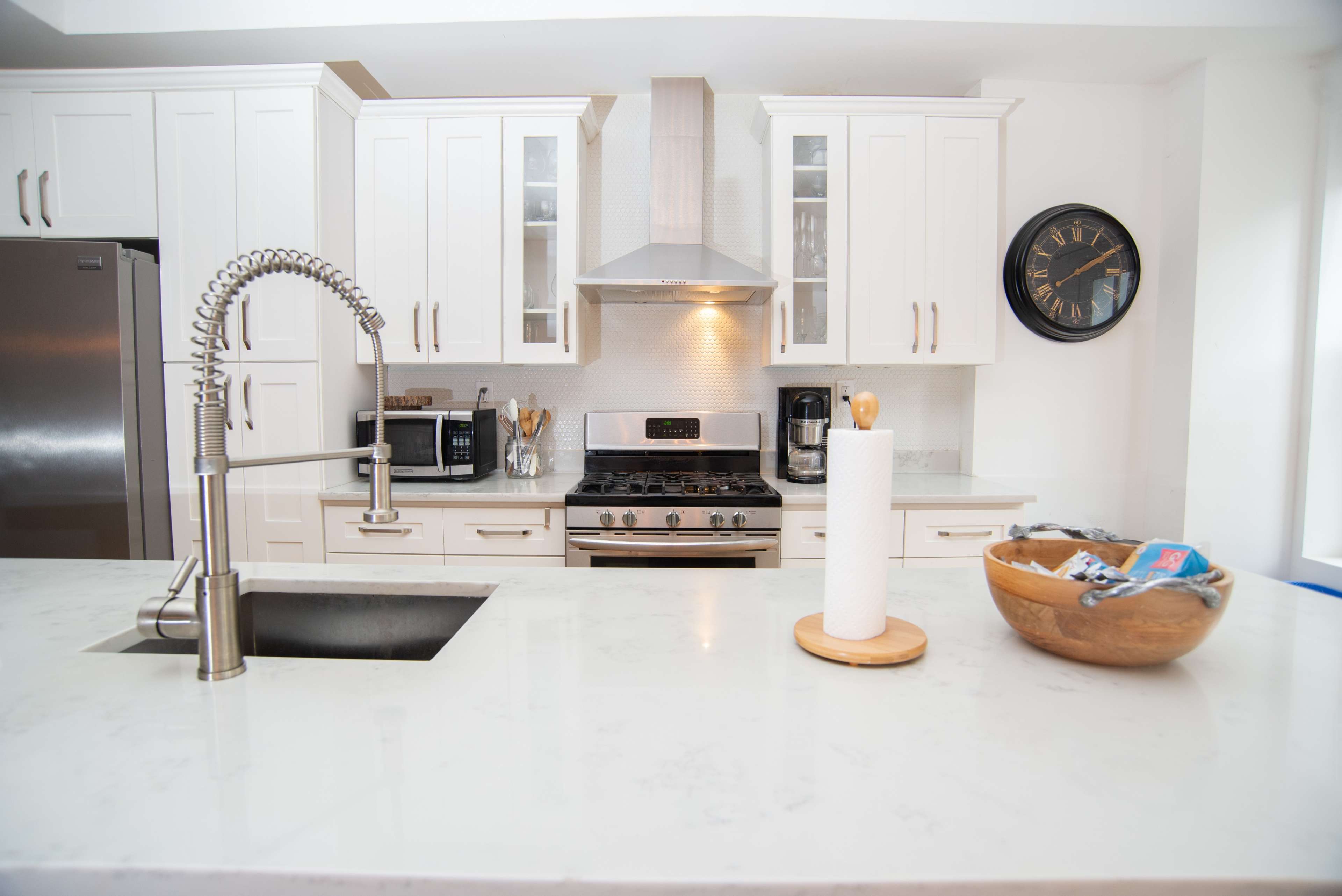 A modern kitchen with white cabinets, stainless steel appliances, a central island with a sink, and a wooden bowl on the counter.