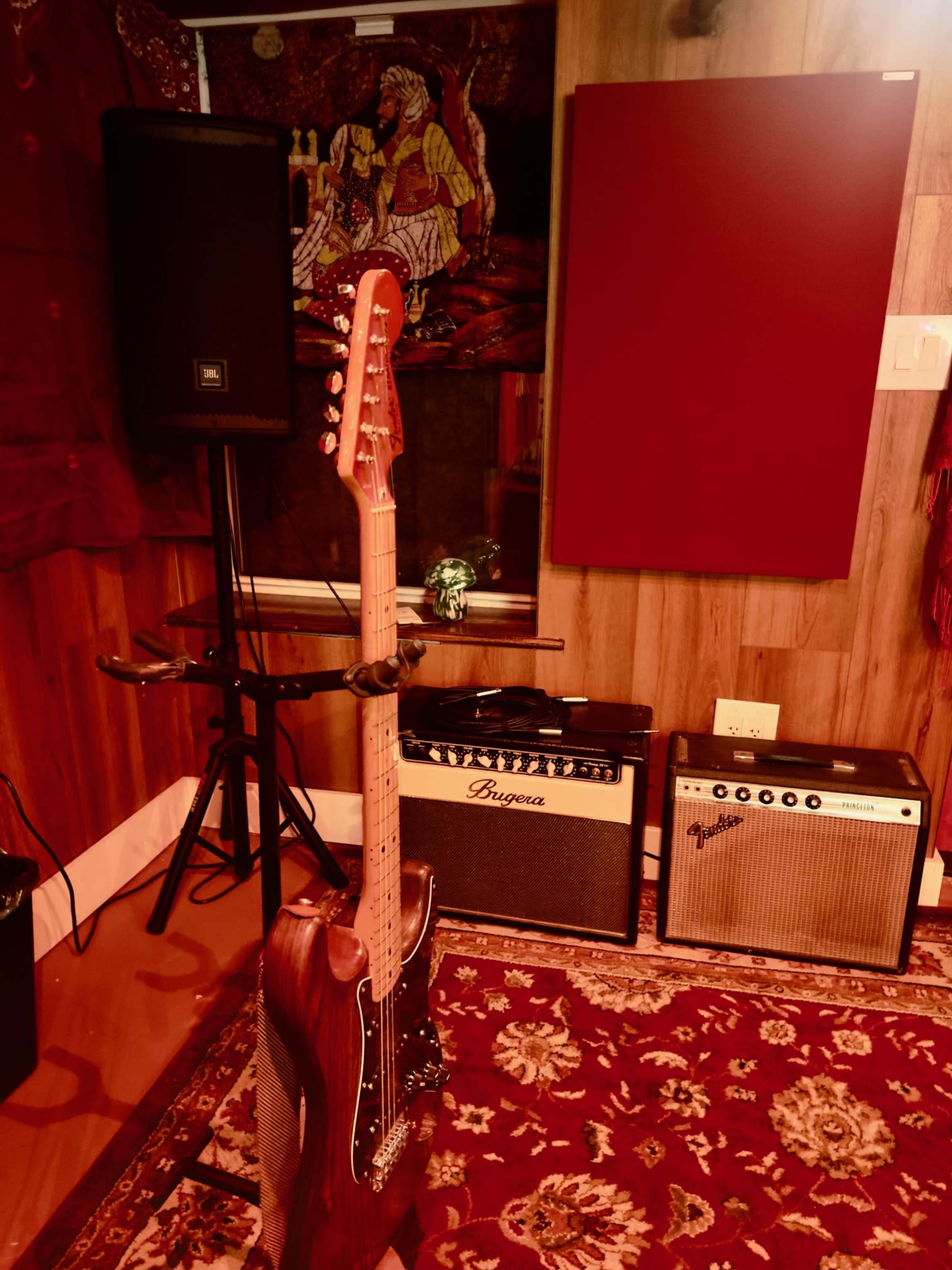 A vintage electric guitar stands on a stand in a music studio with amplifiers and a carpeted floor.