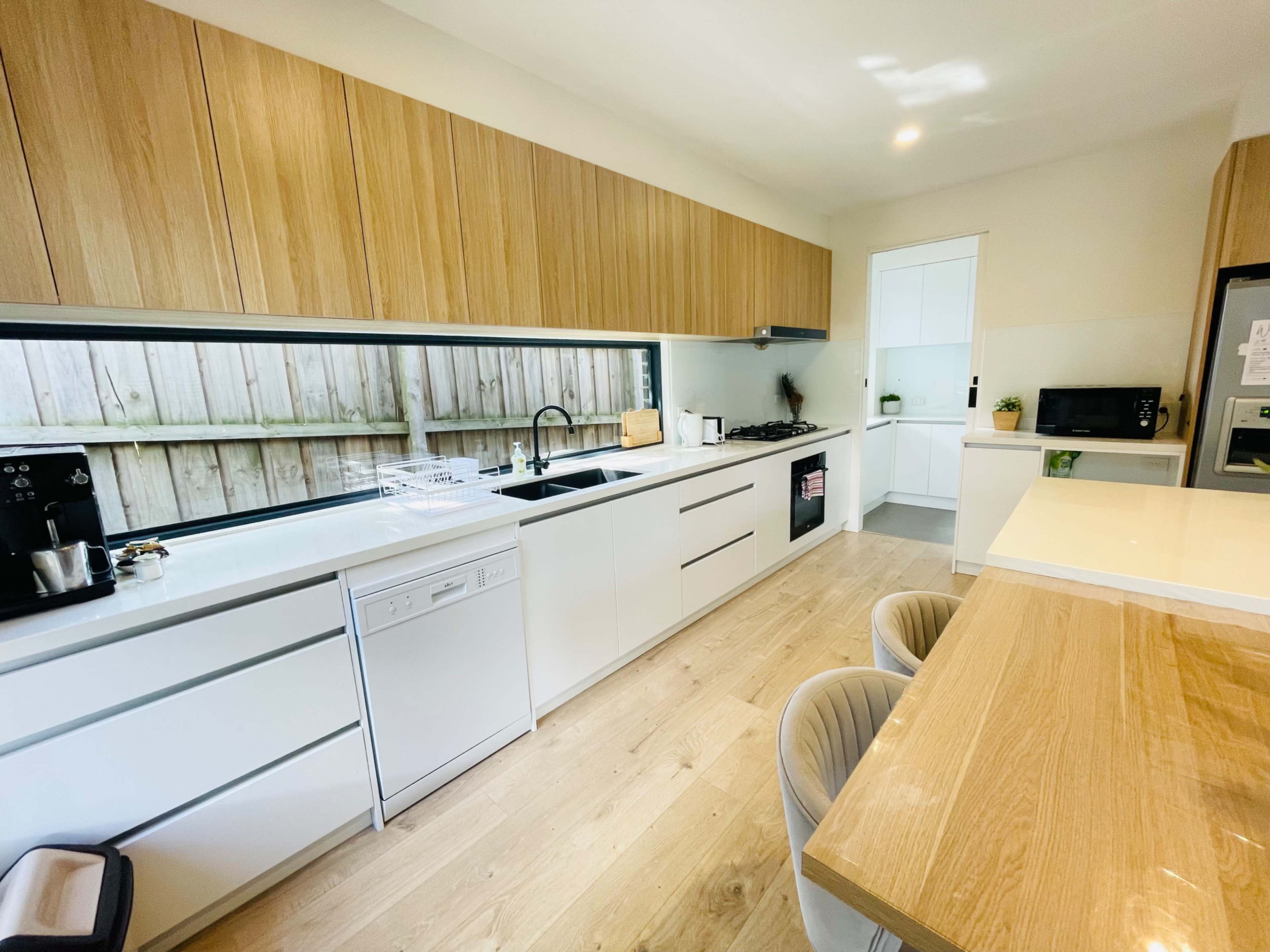 A modern kitchen features sleek white cabinets, wooden accents, and a functional layout with a dining table at one end.