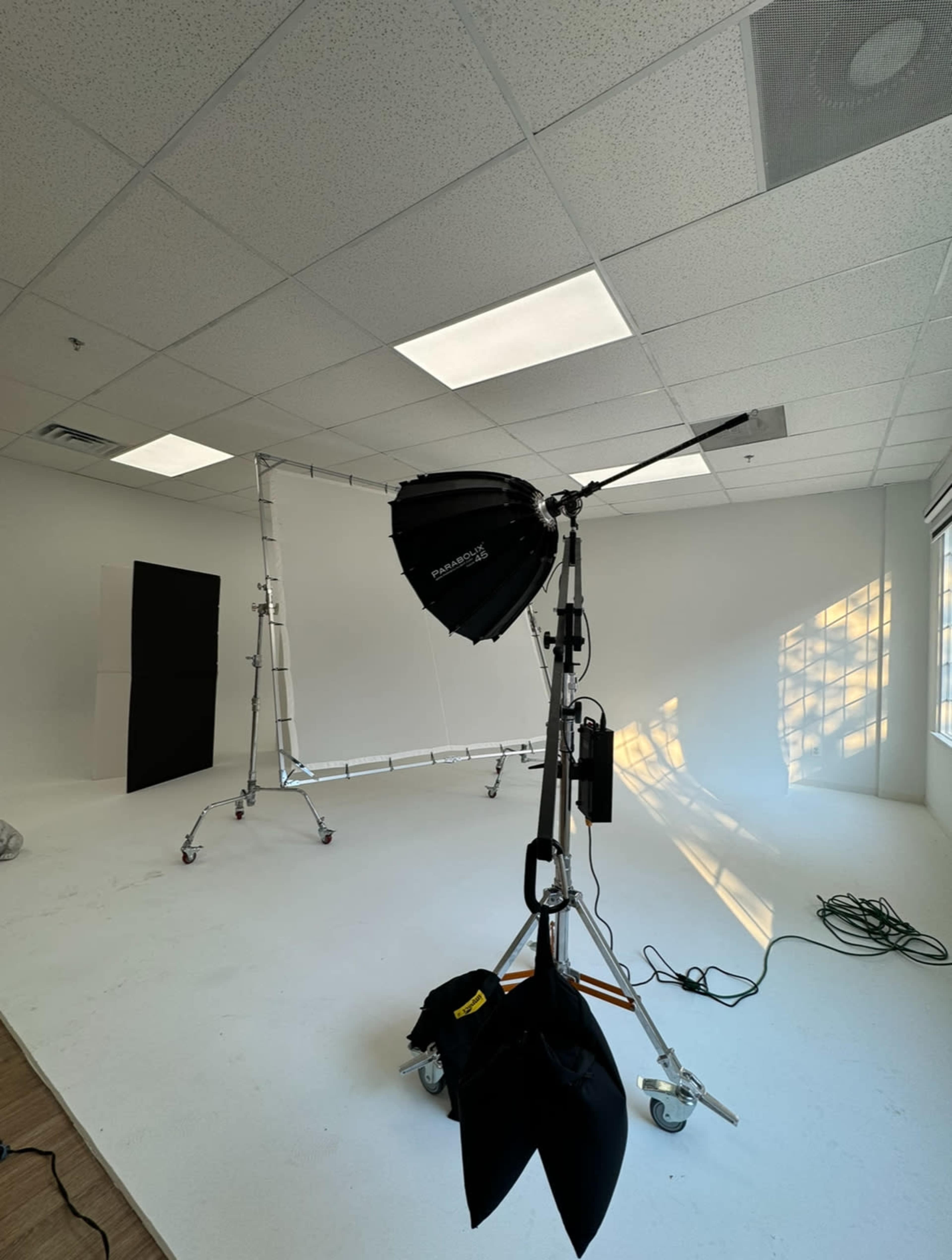 A photography studio with a backdrop setup, a light source on a stand, and various equipment arranged on a white floor.