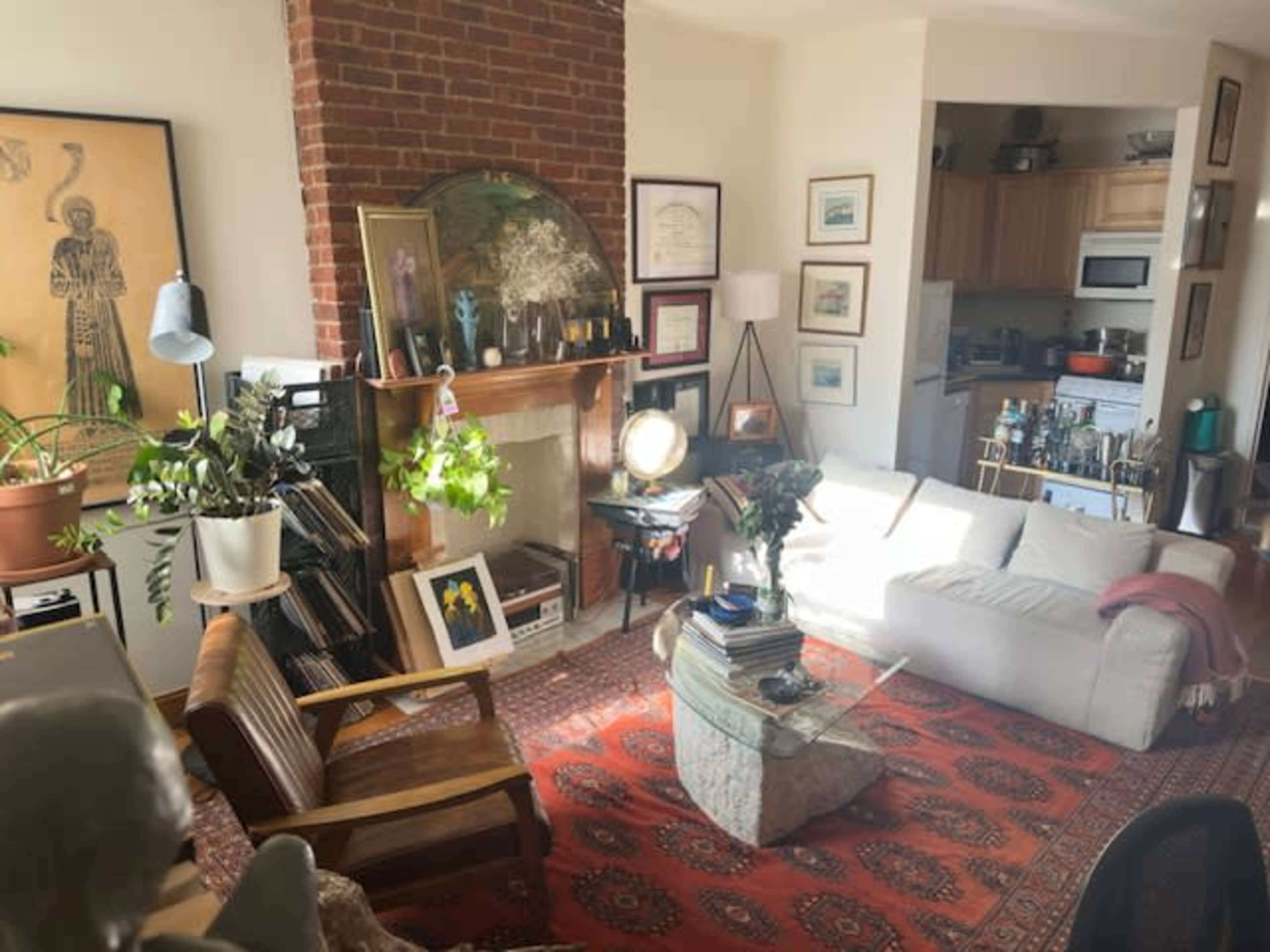 The image depicts a cozy living room with a brick fireplace, a white sofa, and various decorative items on the walls and shelves.