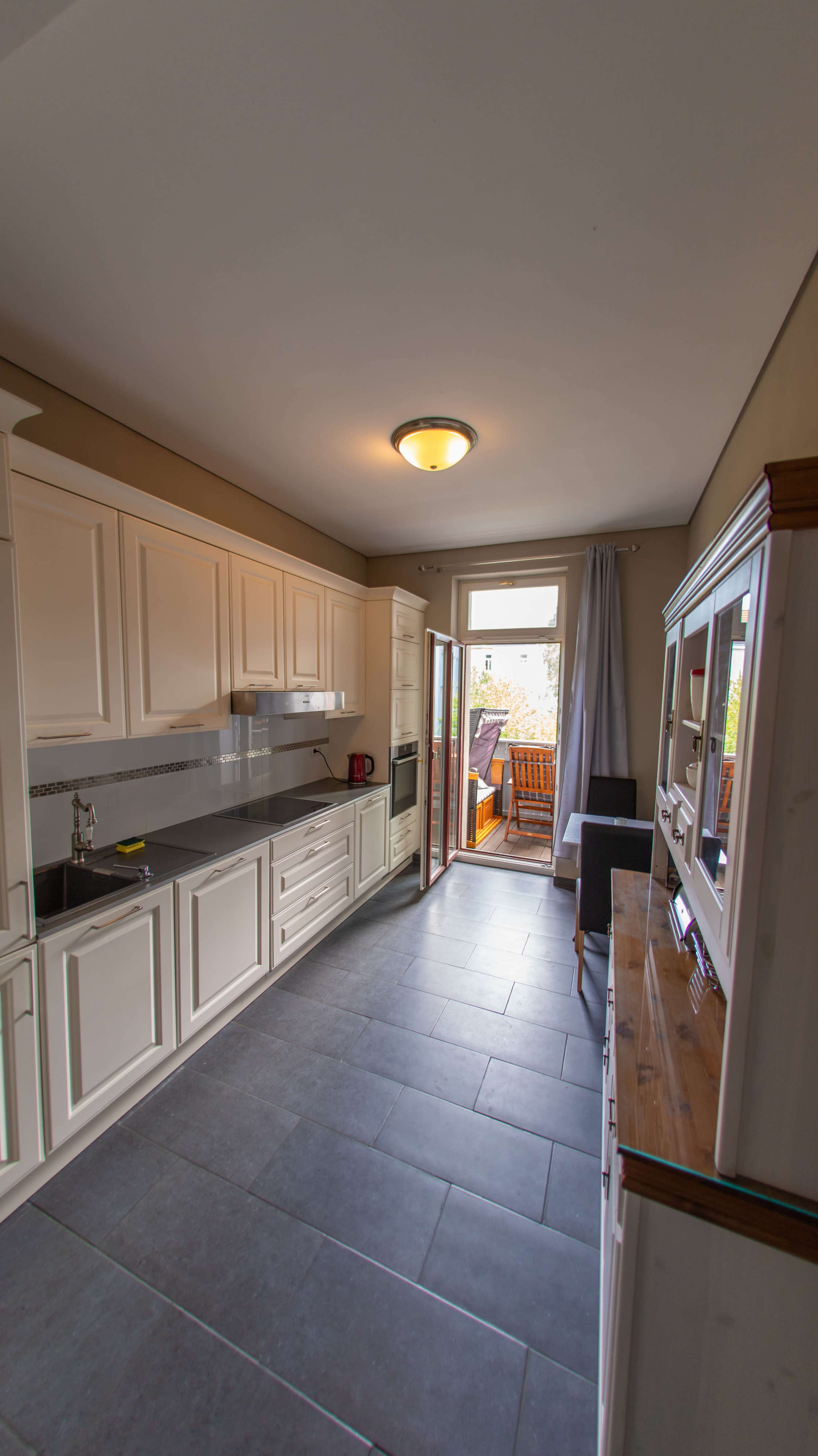 The image shows a modern kitchen with white cabinets, a dark countertop, and a doorway leading to a patio area.