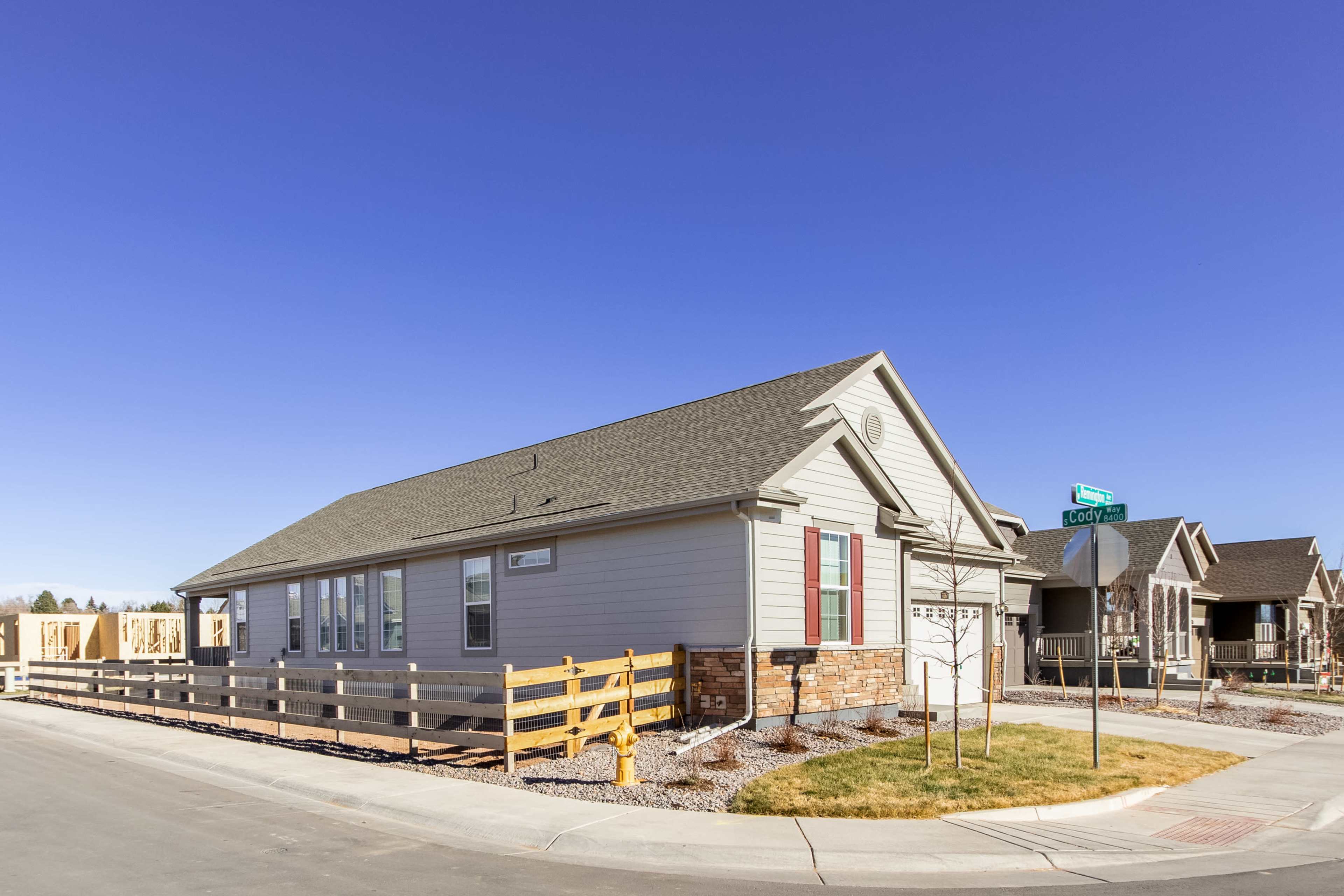 A single-story house with a gray exterior and a fenced yard is situated at the corner of a residential street.