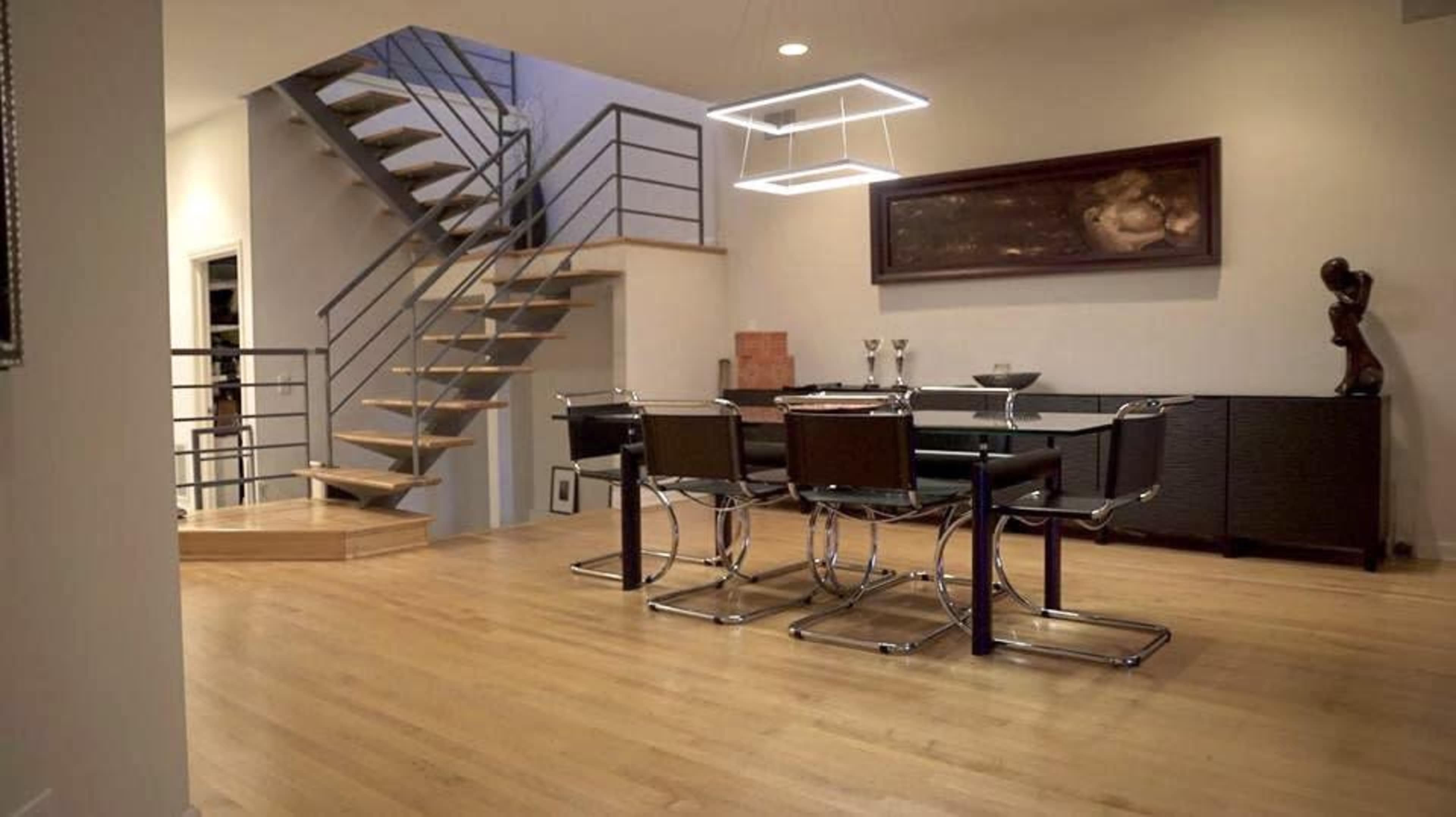 A modern dining area with a glass dining table and black chairs, adjacent to a staircase with wooden steps.