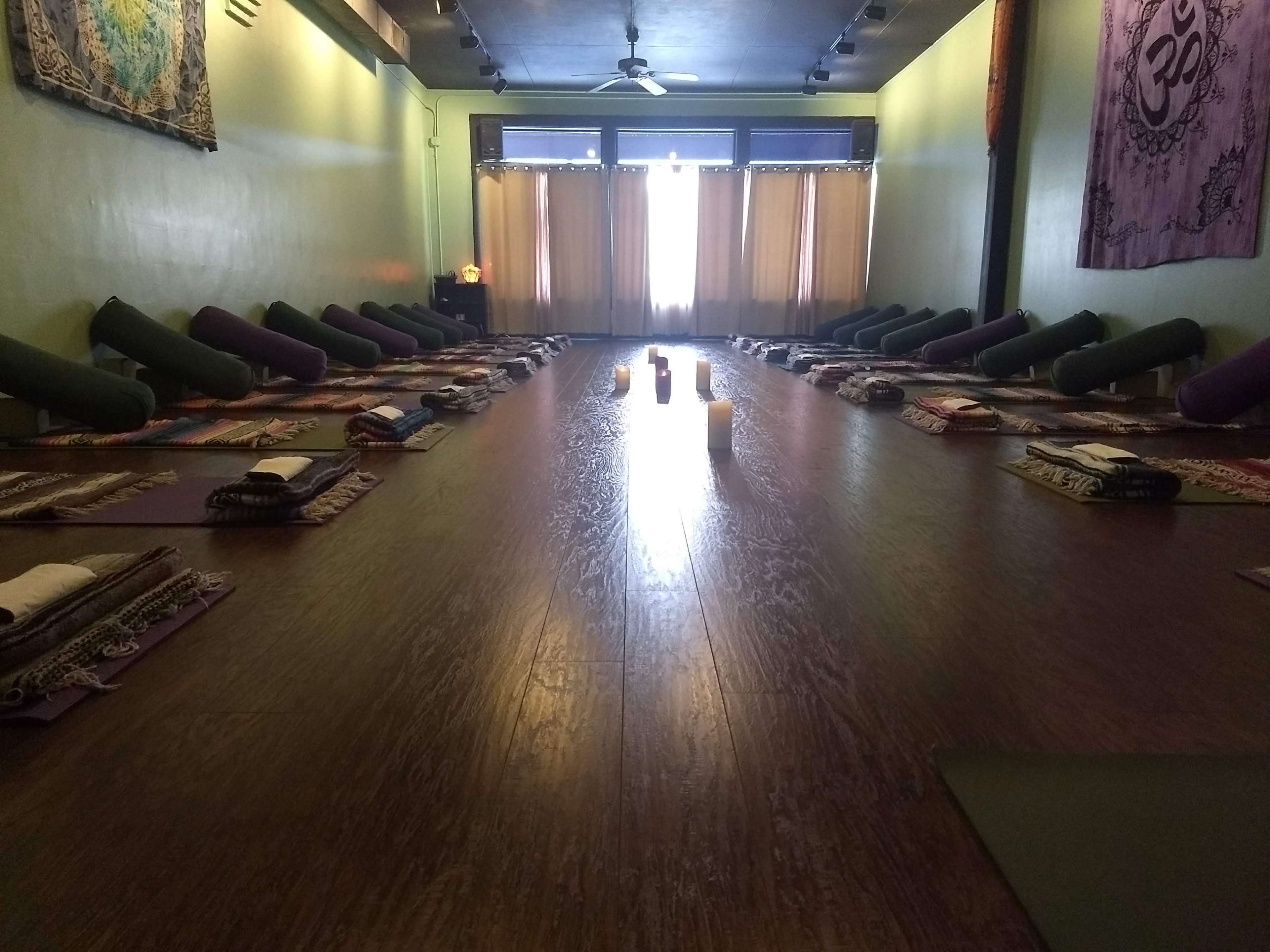 A yoga studio arranged with yoga mats and props in neat rows facing a large window with natural light.