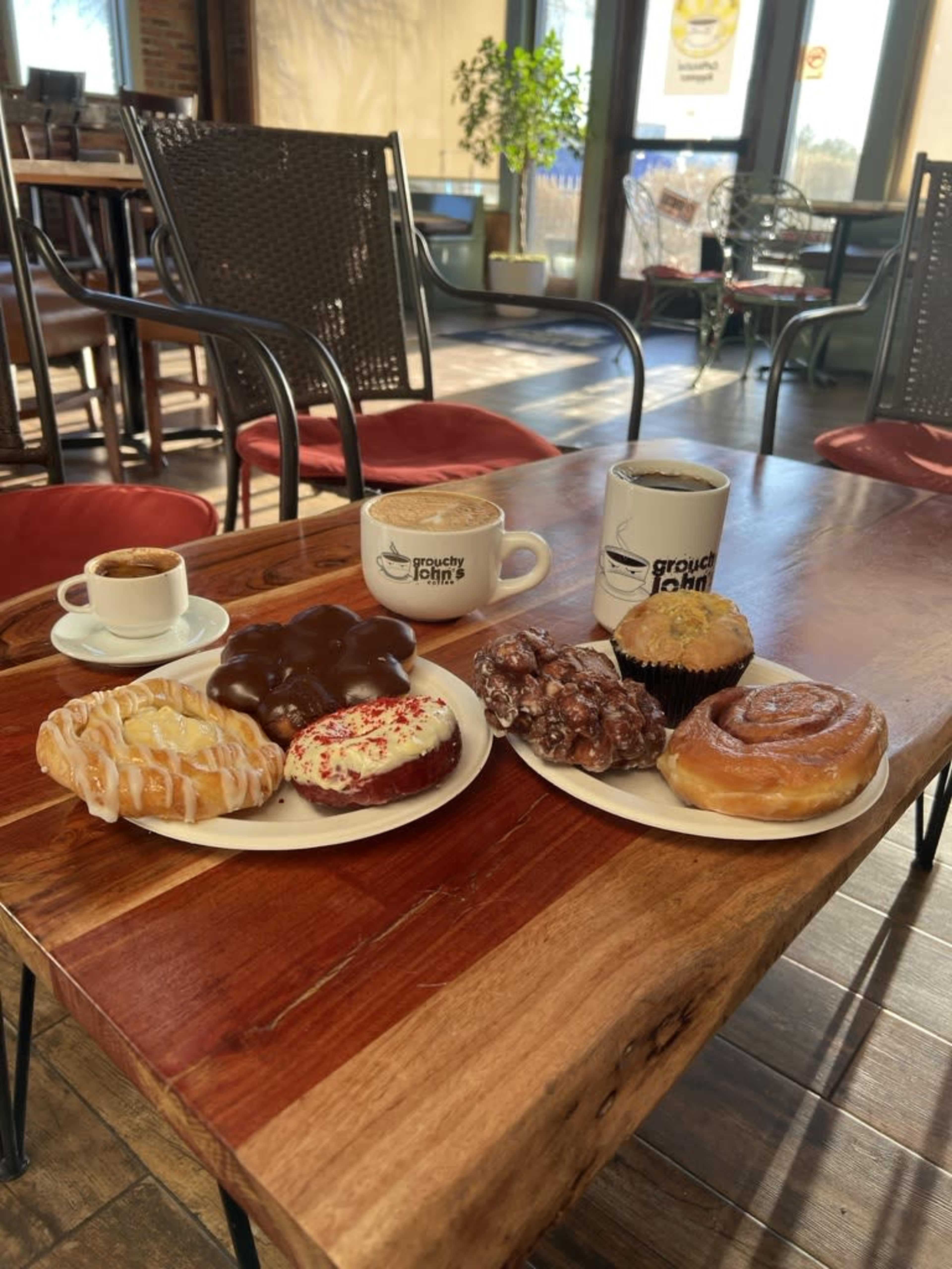 Two plates of assorted pastries and coffee cups are arranged on a wooden table inside a café.