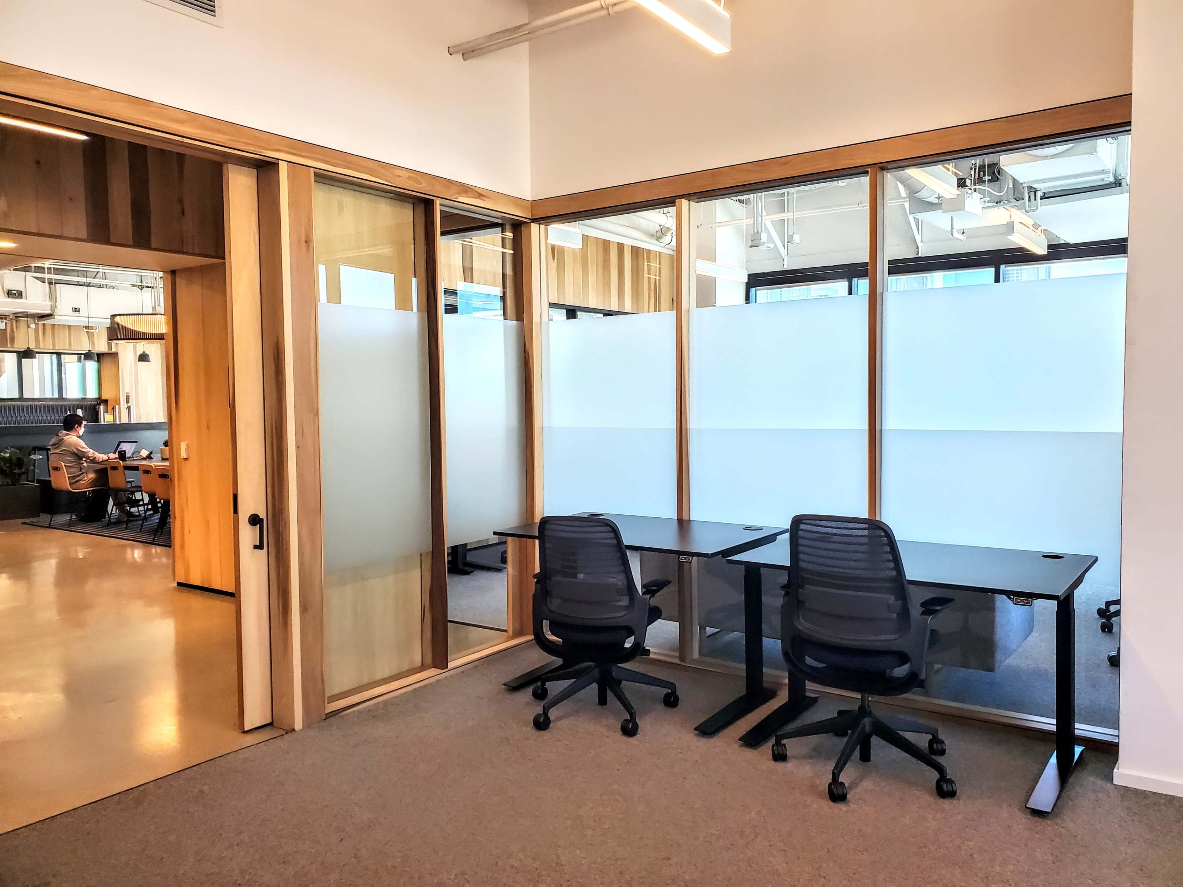 An office space with two desks and a glass-walled meeting room that has a frosted privacy film.