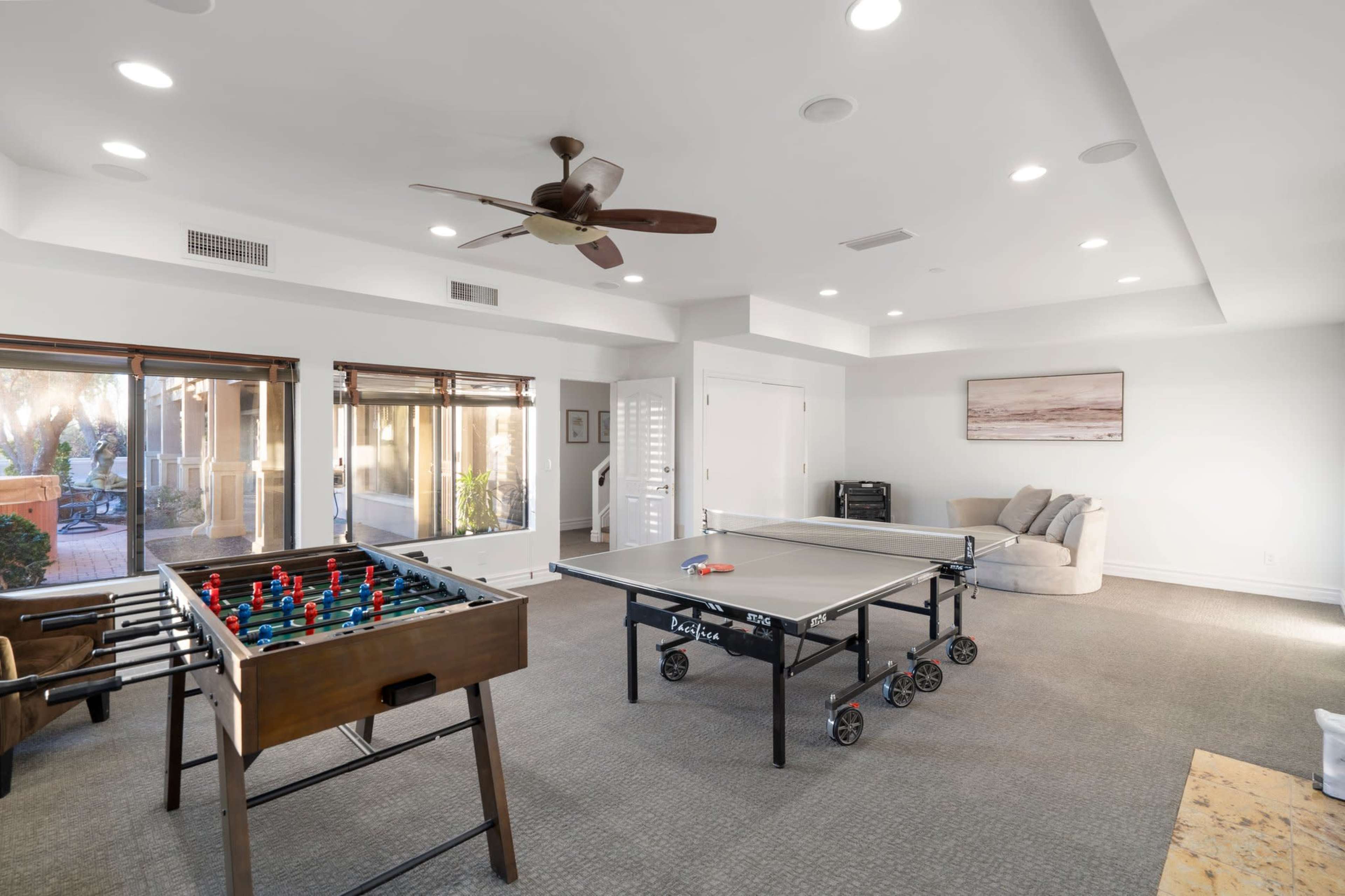 The room features a foosball table and a ping pong table, with large windows allowing natural light to enter.