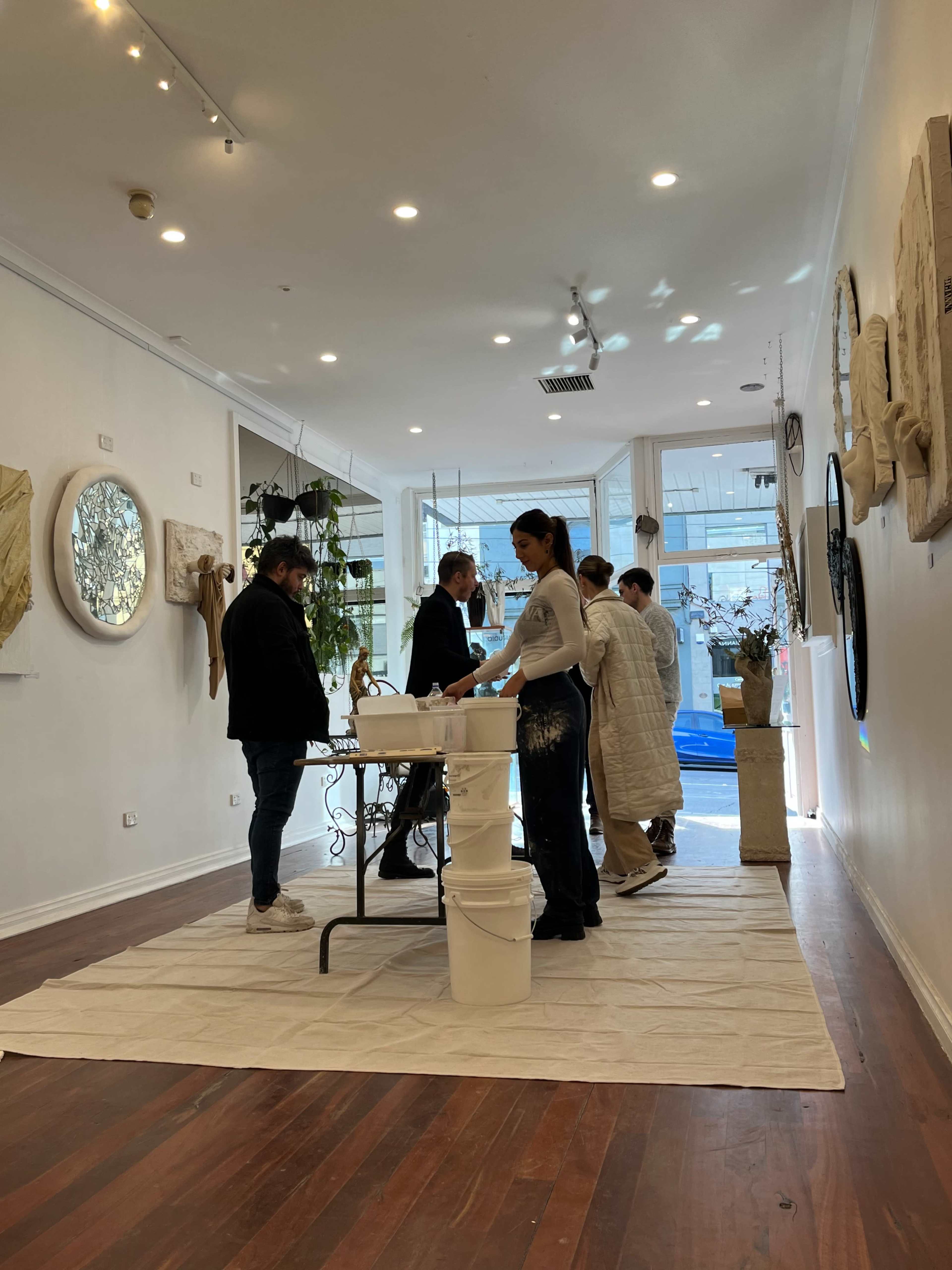 A group of five people engages in an activity inside a spacious art gallery with white walls and wooden flooring.