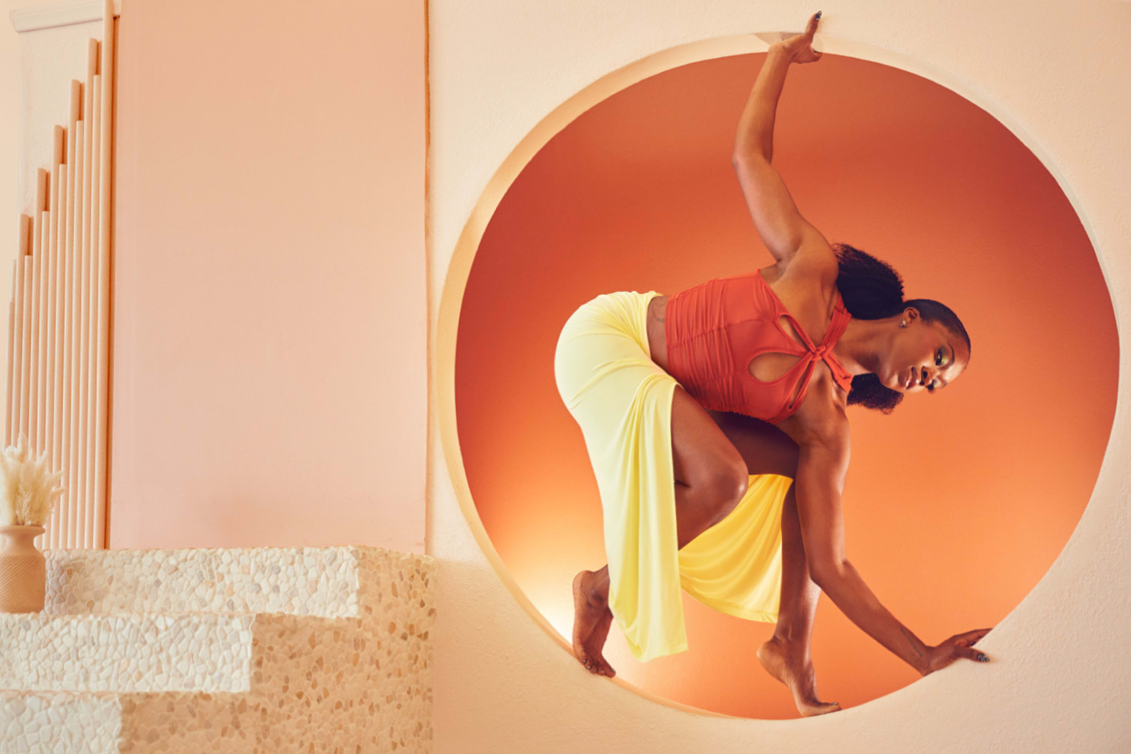 A woman is posing in a circular window during an orange and beige photoshoot.